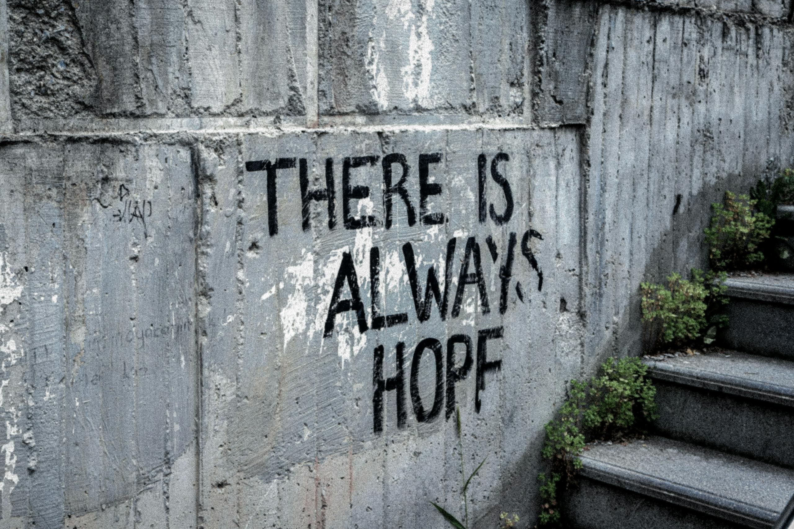 Graffiti on concrete wall reads 'There is always hope' next to outdoor stairs.
