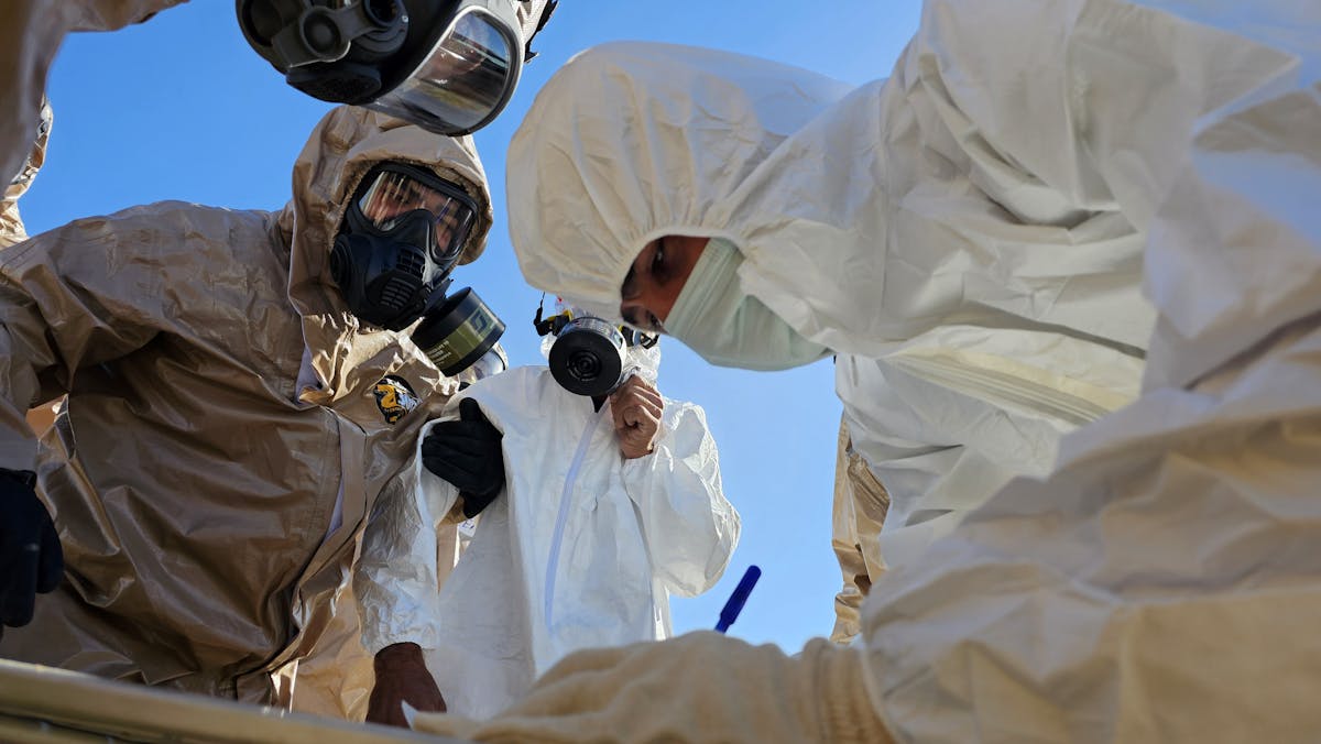 Group of technicians wearing hazmat suits and gas masks during an outdoor inspection.