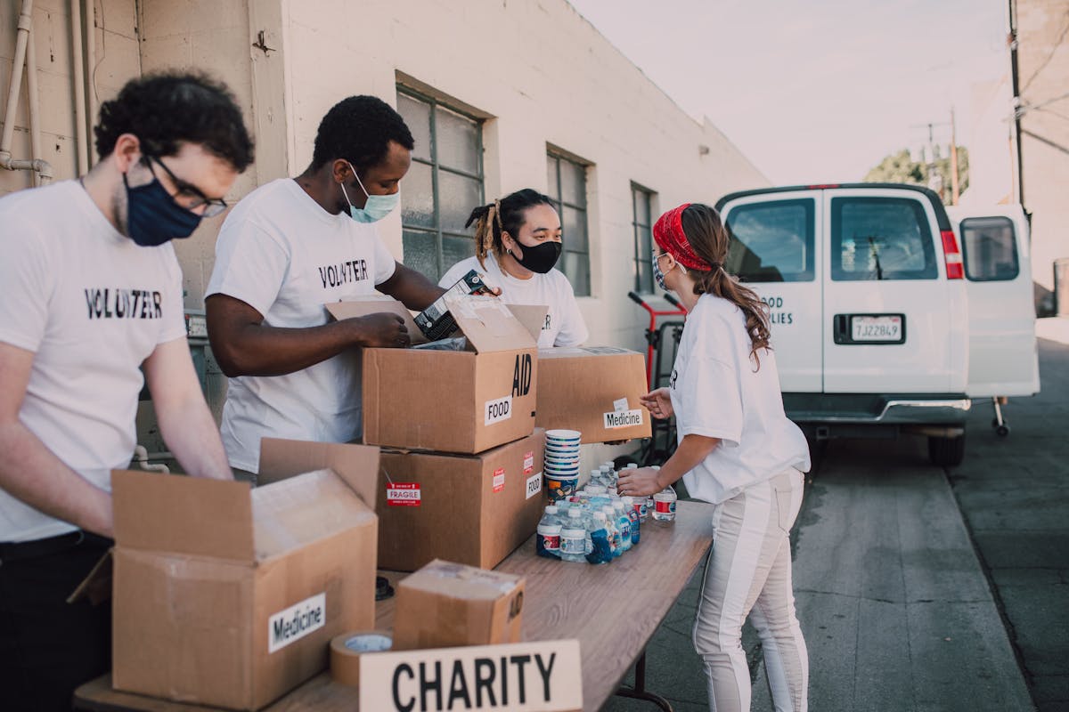 Group of volunteers wearing masks packing charity boxes outdoors during the pandemic.