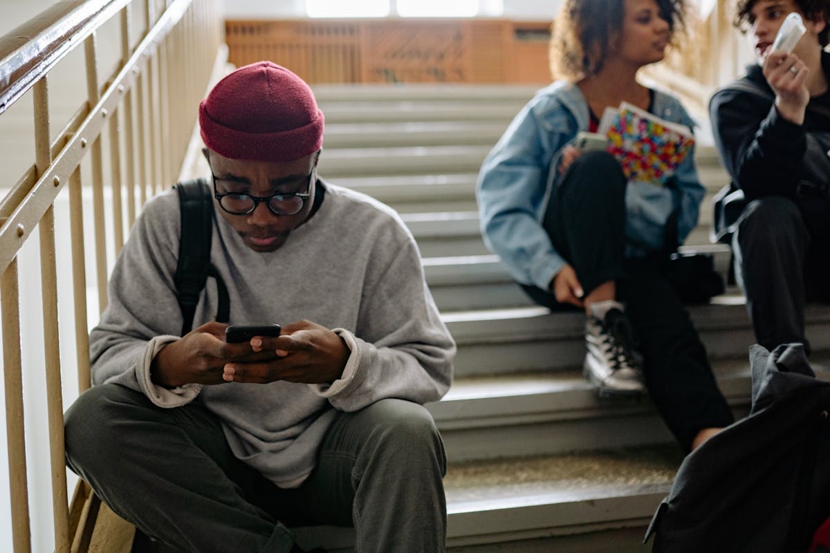 10 Gen Z Habits That Quietly Irritate Millennials 4 Group of young adults sitting on stairs, engaged with smartphones while relaxing indoors.