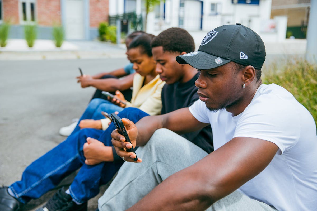 Group of young adults using smartphones seated outdoors in Brussels, capturing modern tech engagement.