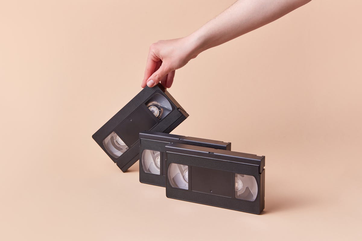 Hand holding a vintage VHS tape with a retro collection against a beige background.