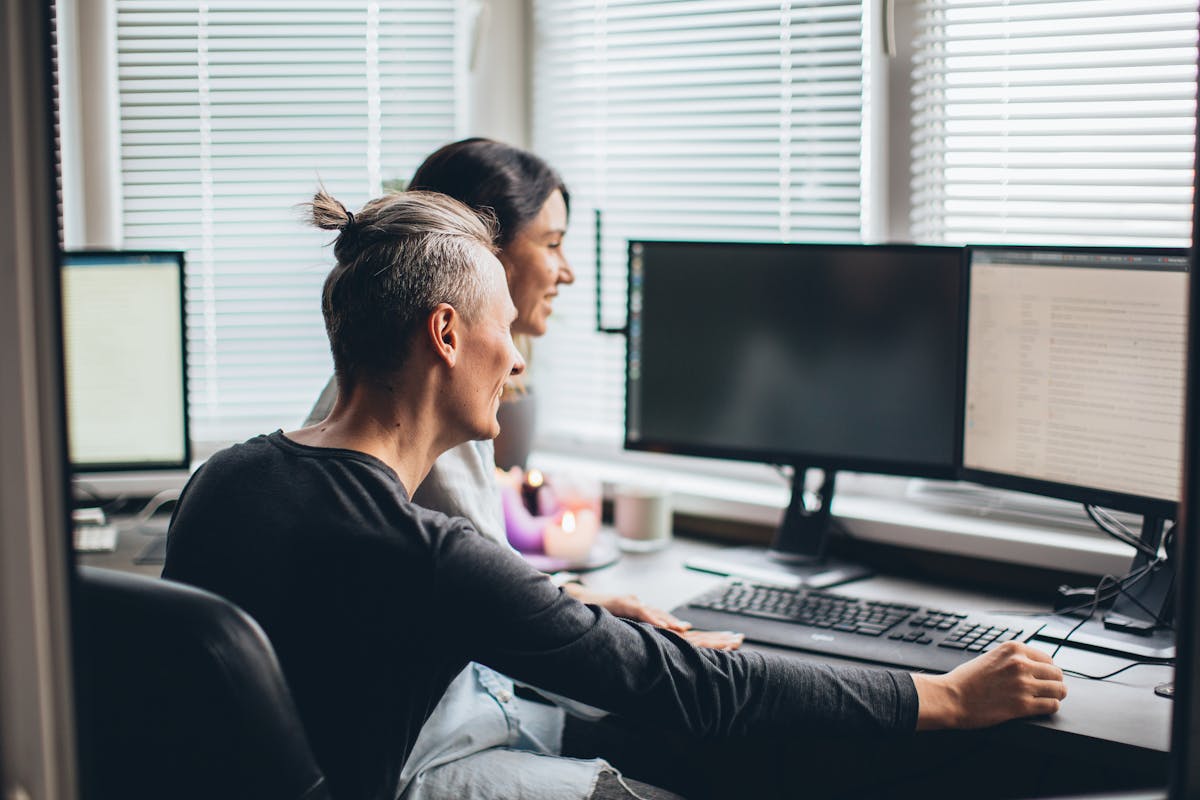 Joyful couple collaborating in a home office setting with computers and natural lighting.