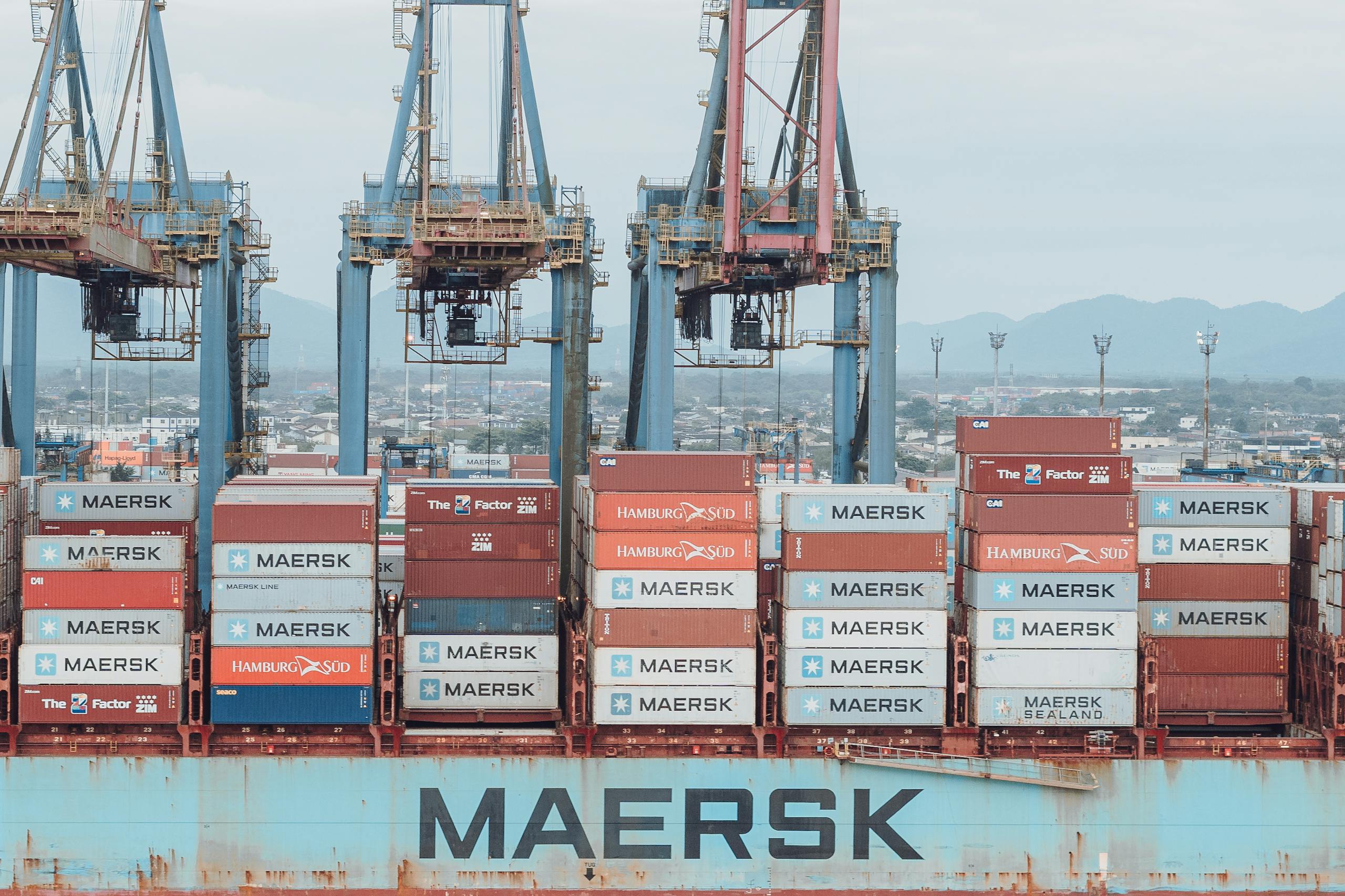Large cargo ship loaded with shipping containers at a busy industrial port.