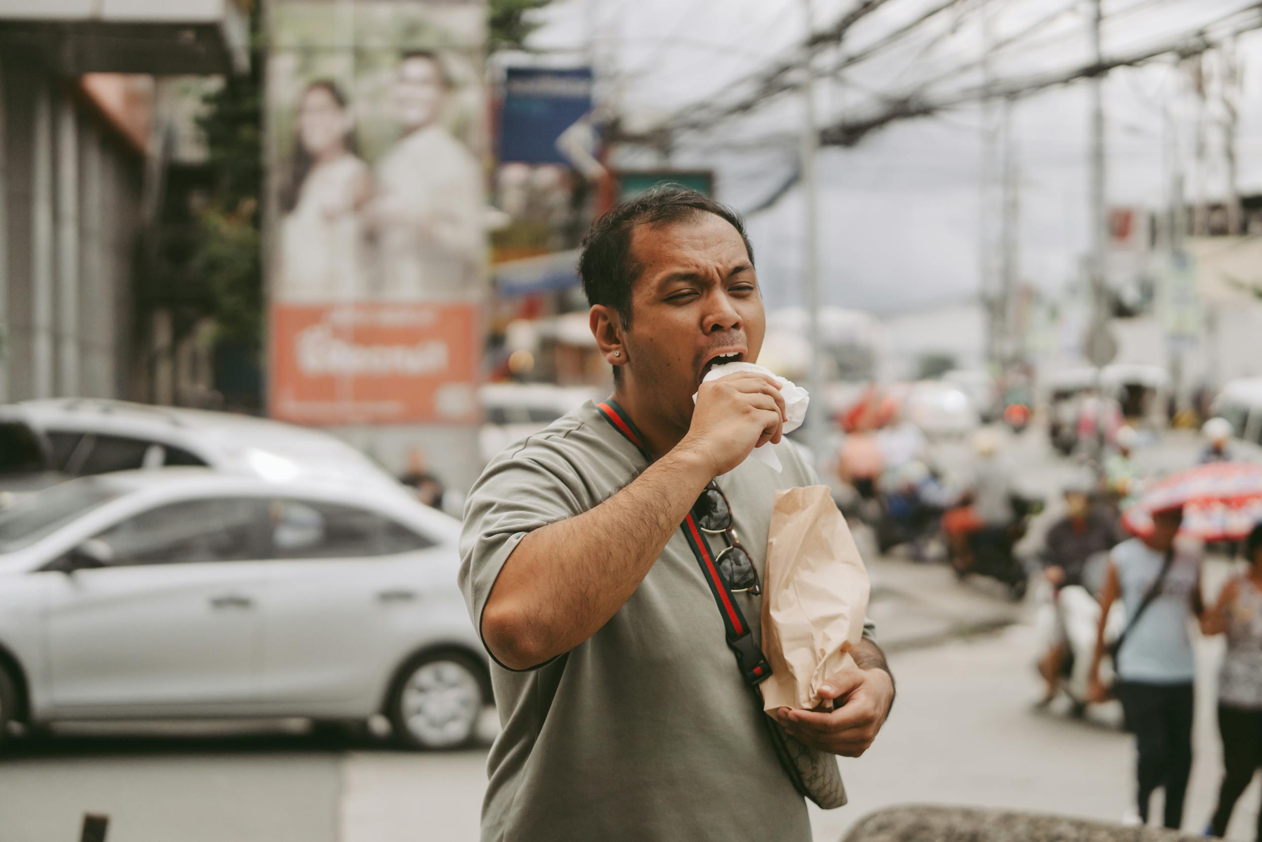 10 Public Habits That Make Strangers Hate You 1 Man enjoying street food amidst a busy city scene with cars and pedestrians.