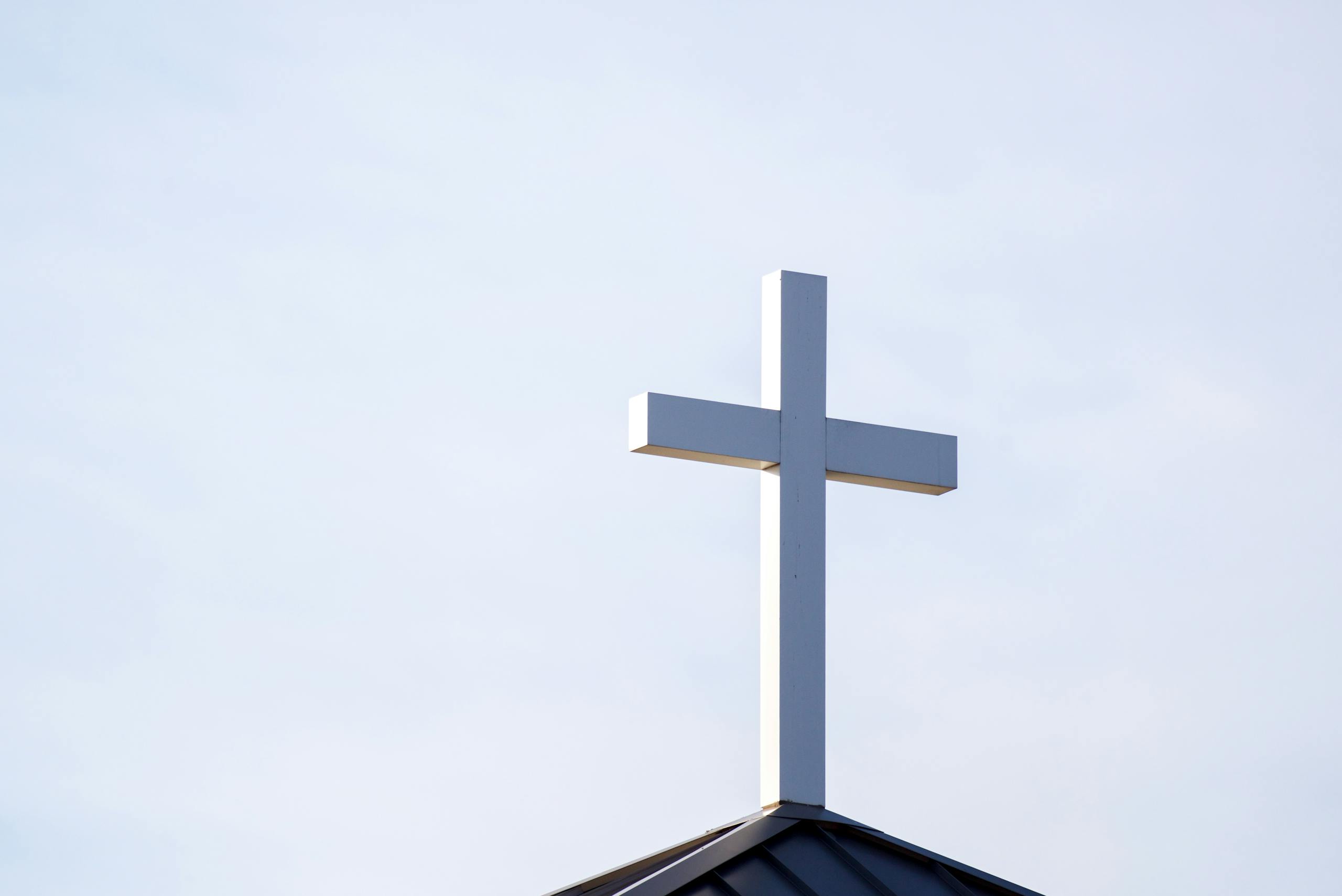7 Ways America’s Immigration Fight Is Tearing Ordinary Communities Apart 2 Minimalist image of a white cross on a church roof against a clear blue sky.