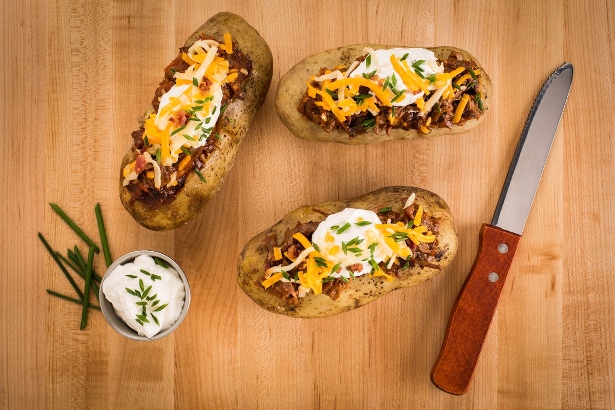 10 Cheap Summer Meals That Keep Families Fed Without Breaking the Bank or Losing Their Minds 2 Mouth-watering loaded baked potatoes with cheese, sour cream, and chives on a wooden surface.