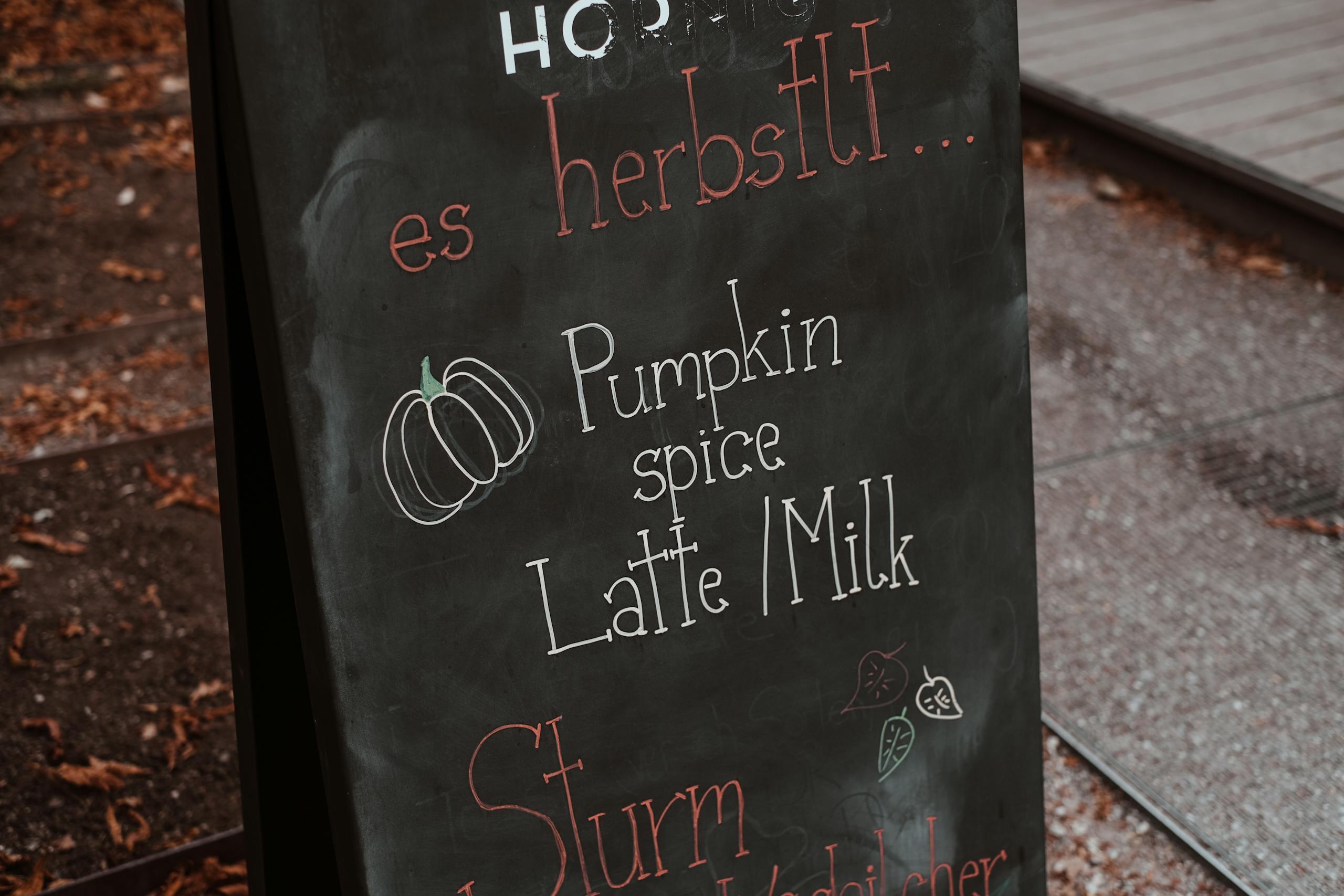 Outdoor chalkboard menu featuring pumpkin spice latte milk in autumn setting.