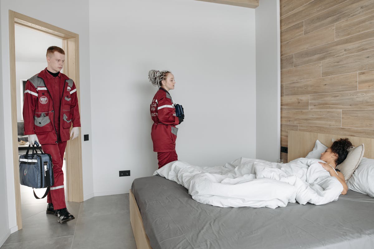 9 Silent Reasons People Die in Their Sleep, According to Science 2 Paramedics assisting an unwell woman lying in bed, showcasing medical intervention indoors.