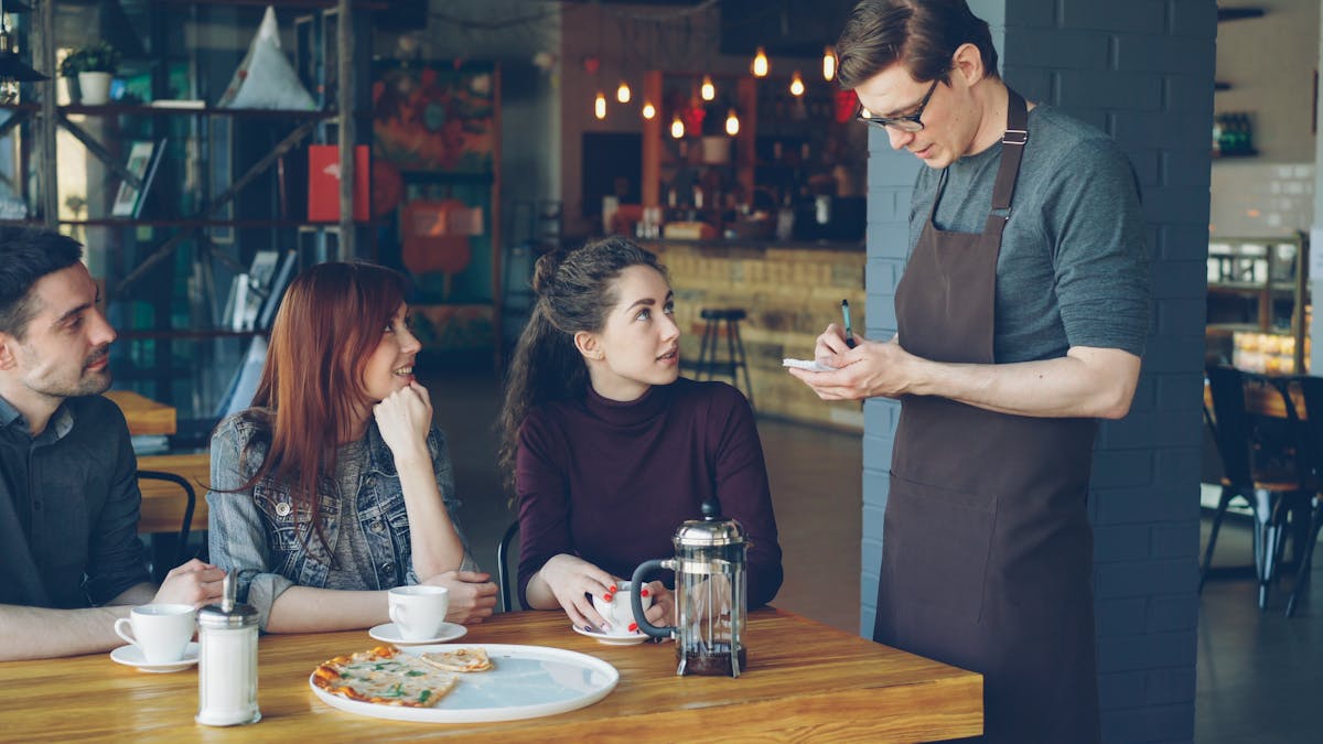 People having a relaxed meeting in a cozy café, interacting with a waiter.