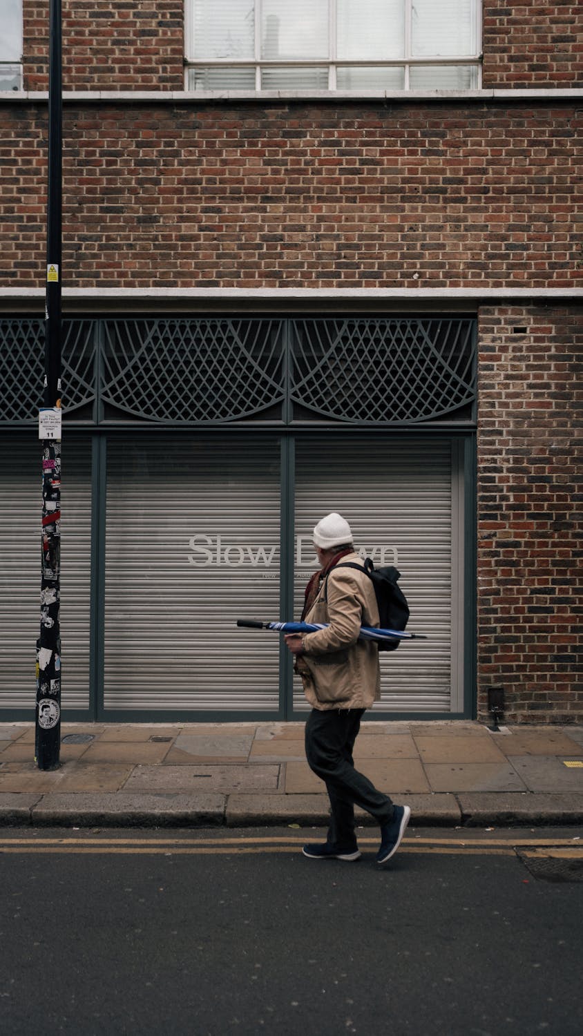 Person walking past a brick building with a closed shopfront on a city street.