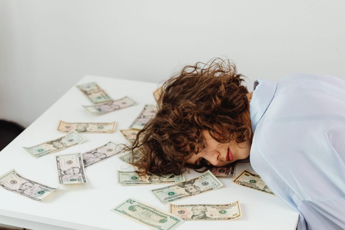 8 Childhood Money Habits That Are Suppressing Your Finances Today 2 close-up-shot-of-a-curly-haired-woman-lying-her-head-on-white-table-with-paper-money