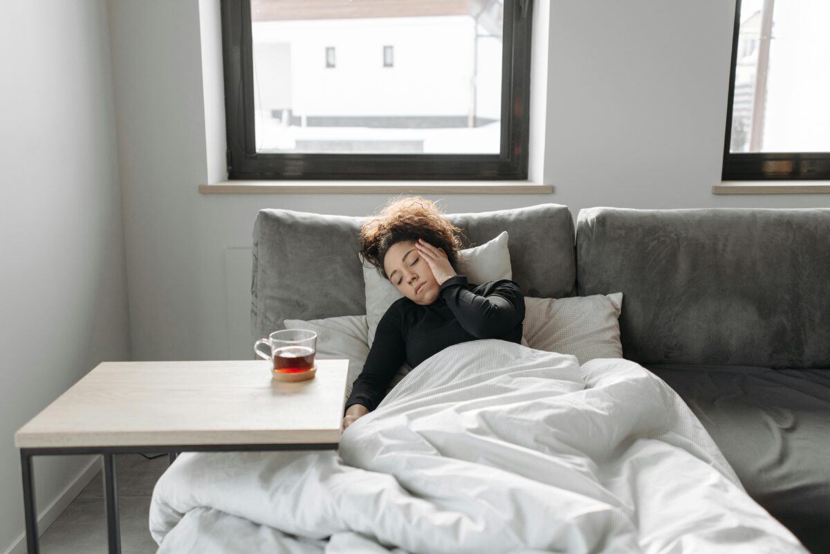 6 Symptoms You Should Never Dismiss as Normal Aging 4 A woman rests on a couch indoors, feeling unwell, with a cup of tea nearby.