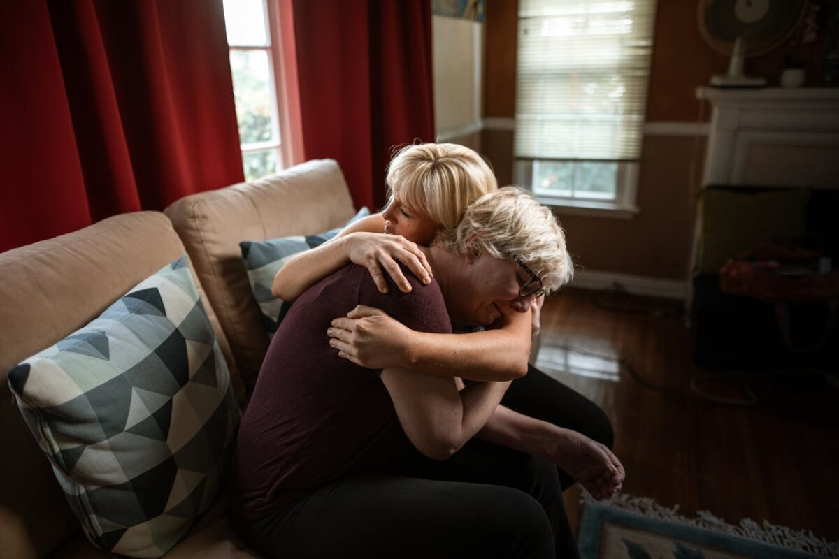 /woman-embracing-crying-elderly-woman-while-sitting-on-couch-