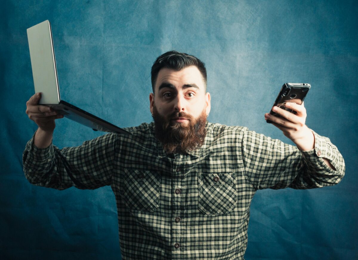 bearded-man-holding-cellphone-and-laptop-on-blue-background