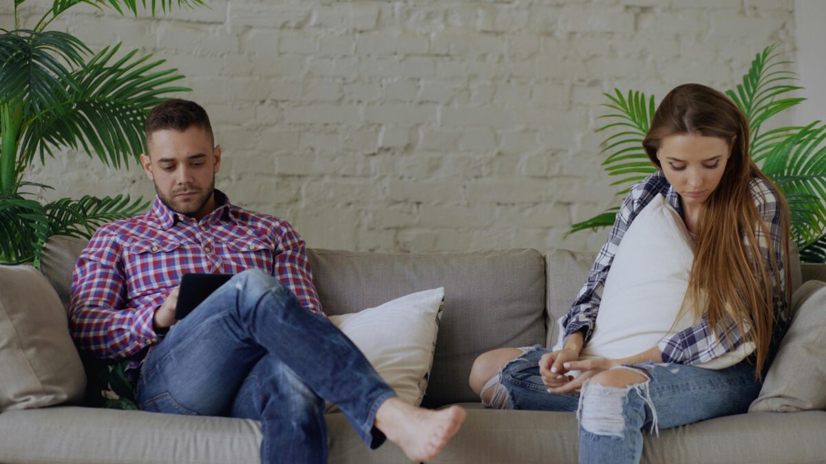 couple-sitting-on-couch-ignoring-each-other-in-living-room