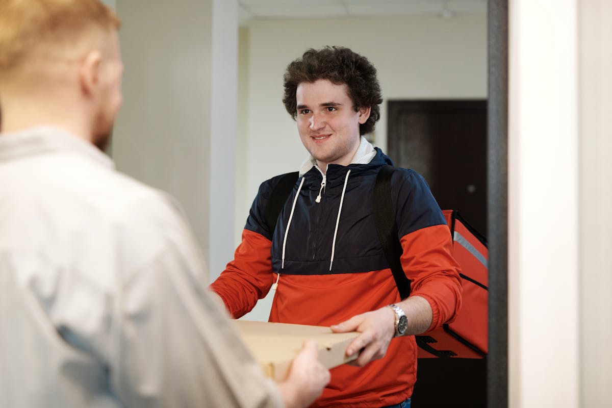 Pizza delivery man in casual wear delivers pizza box to a customer indoors, smiling. receiving takeout from delivery