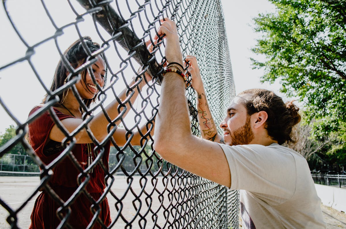 Playful couple enjoying a sunny day outdoors, interacting through a fence.