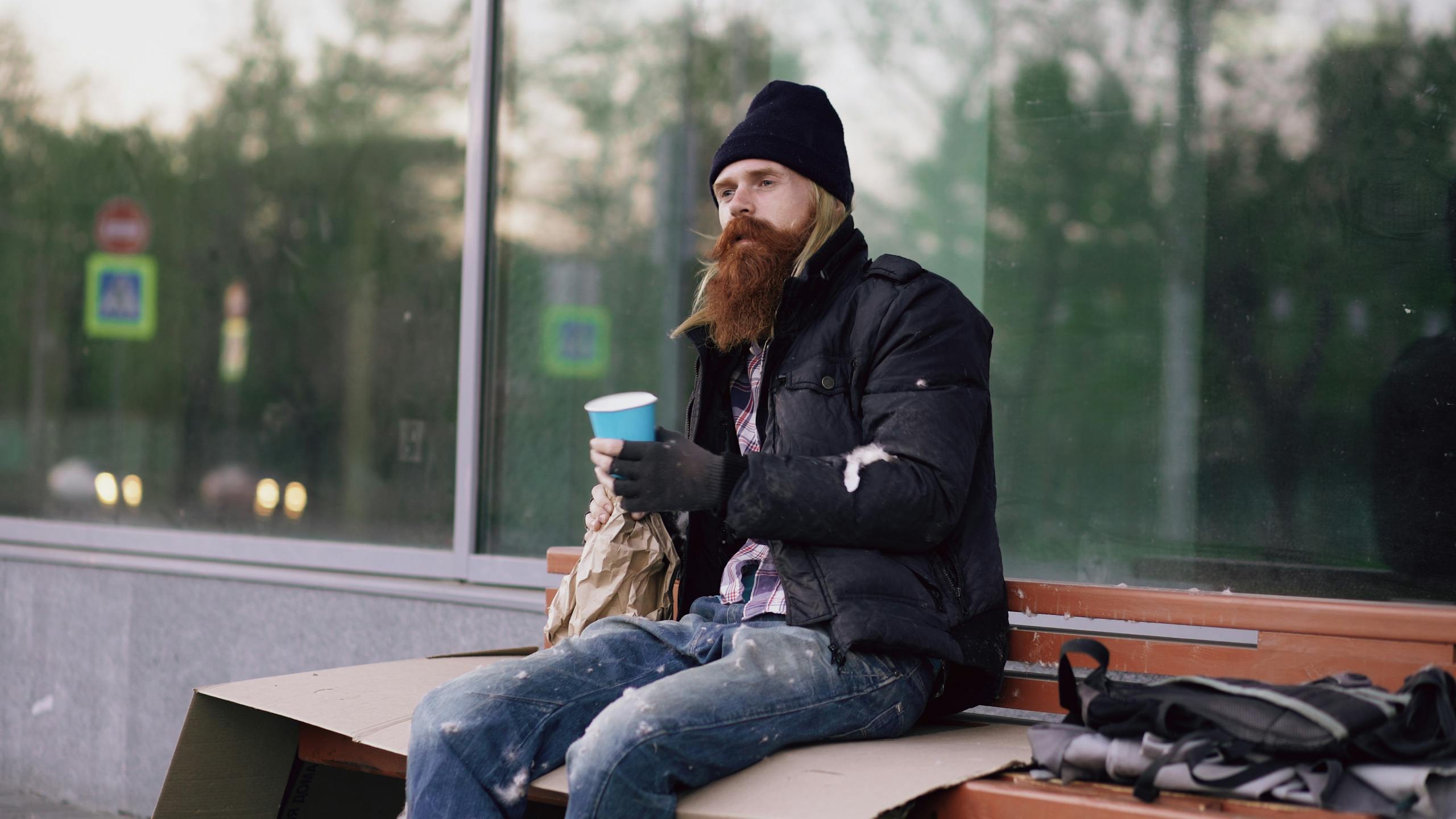 Seattle’s No-Sobriety Shelter Plan Could Test Americans’ Patience on Homelessness and Safety 2 Portrait of a homeless man sitting on a bench holding a cup outdoors.