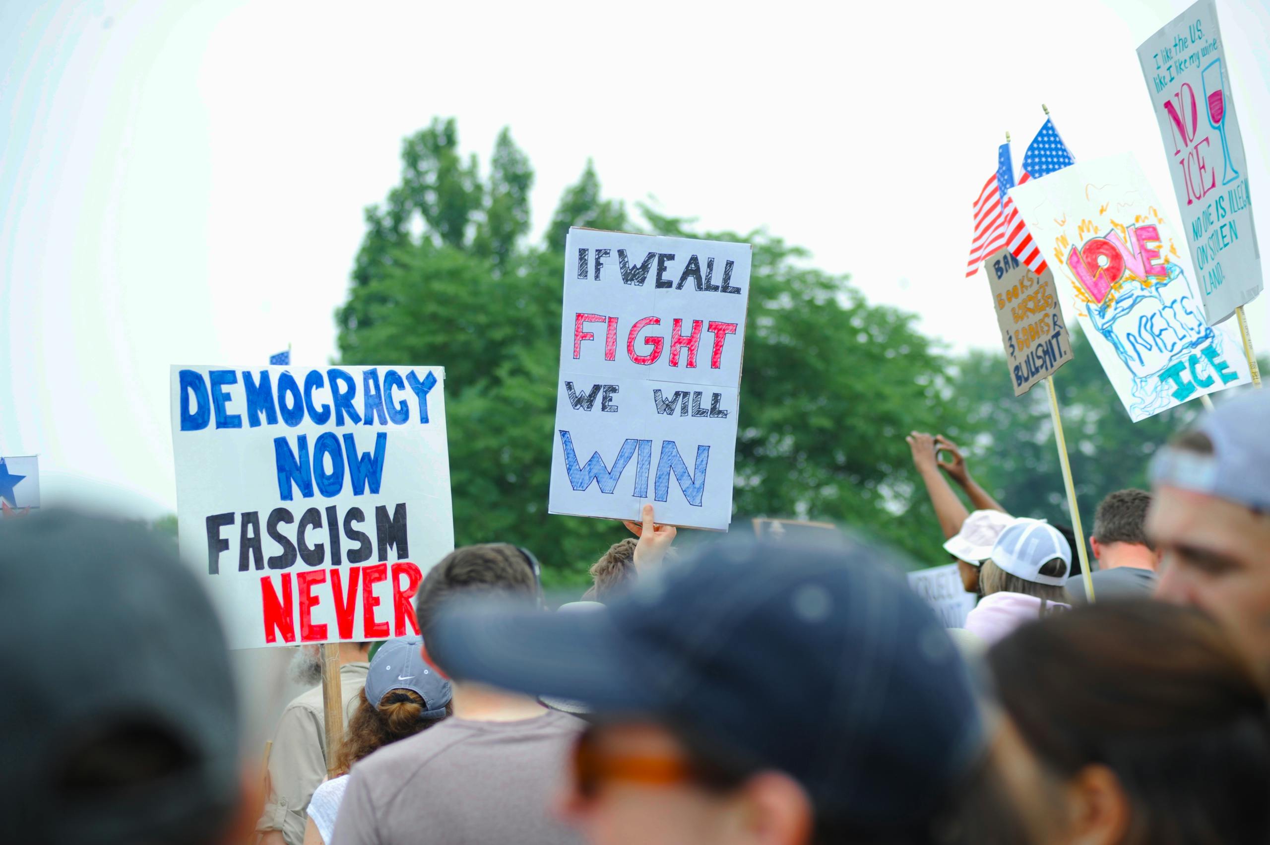 7 Alarming Warnings from Barney Frank That Could Haunt Democrats in 2026 2 Protesters gather with signs advocating democracy and rejecting fascism at a rally in Baltimore.