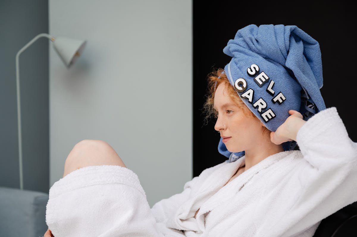 6 Self-Care Myths That Are Doing More Damage Than Most People Realize 4 Relaxed woman in a bathrobe with a towel headwrap featuring 'self care' letters enjoying a moment at home.