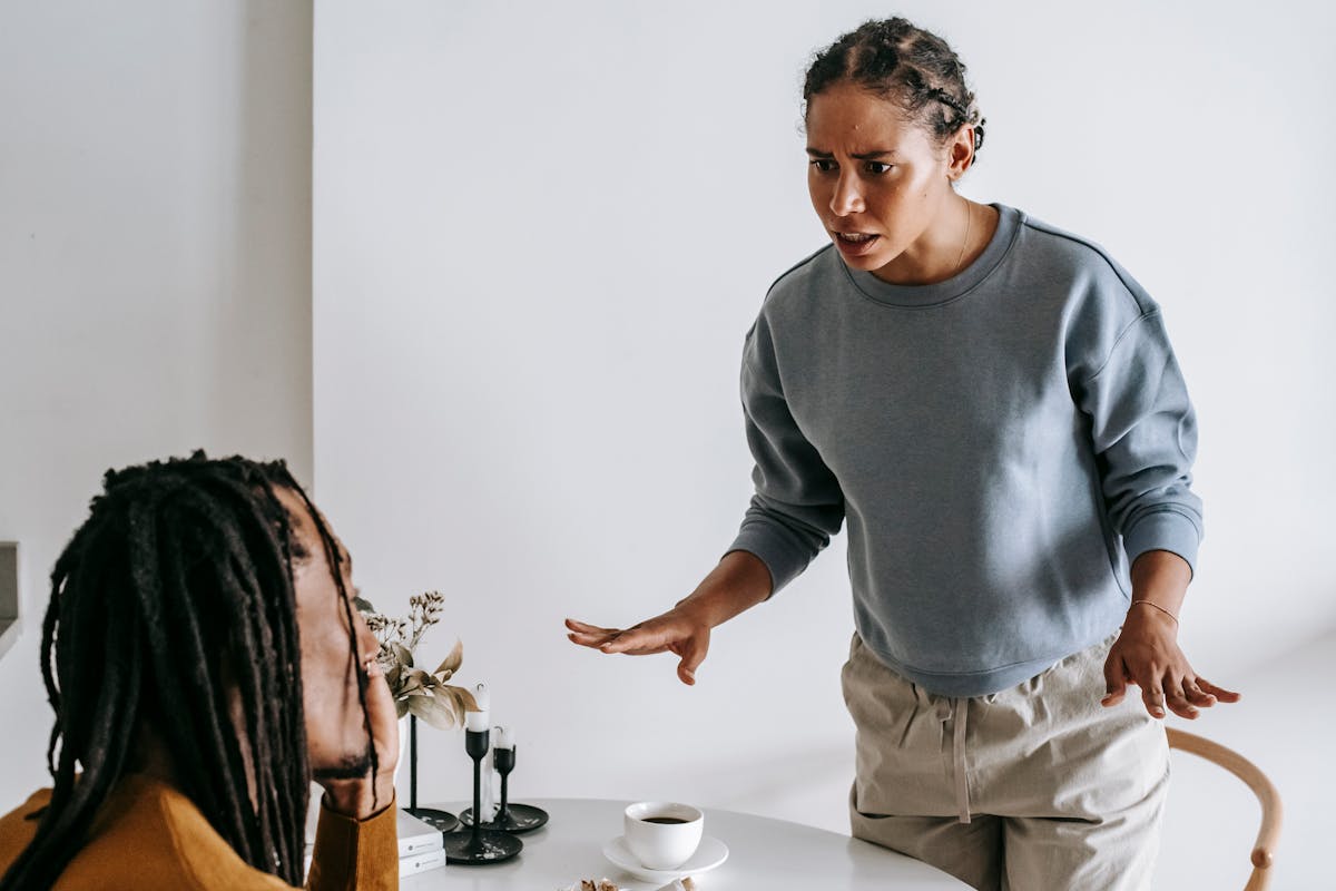 7 Signs Women Quietly Pull Back When Love Turns Into Resentment 3 Serious young African American female in casual outfit standing near round table with cup of coffee and arguing with bearded husband