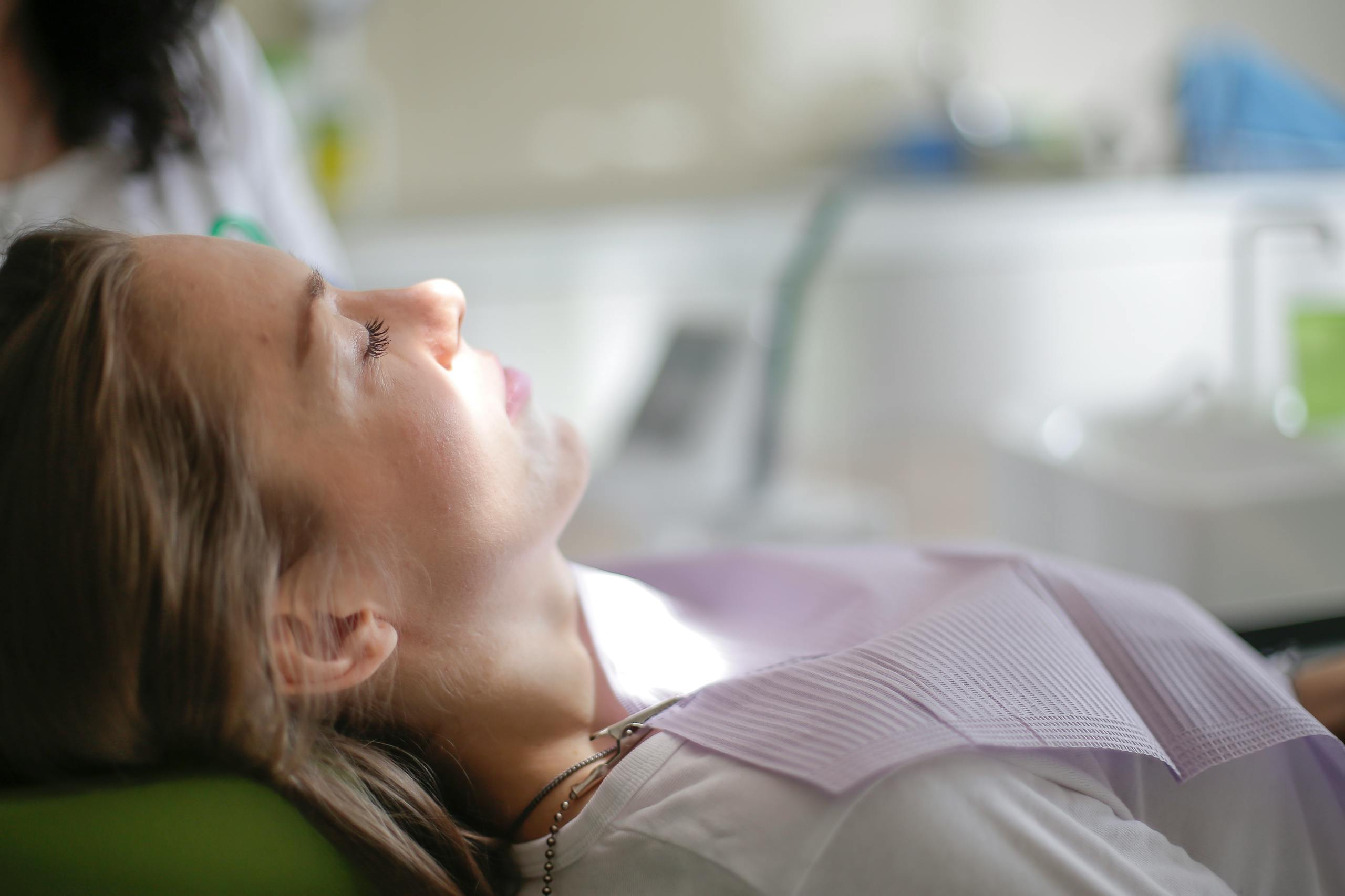 Side view of calm female patient lying with closed eyes and napkin on chest during visit to dentist for treating teeth in modern clinic