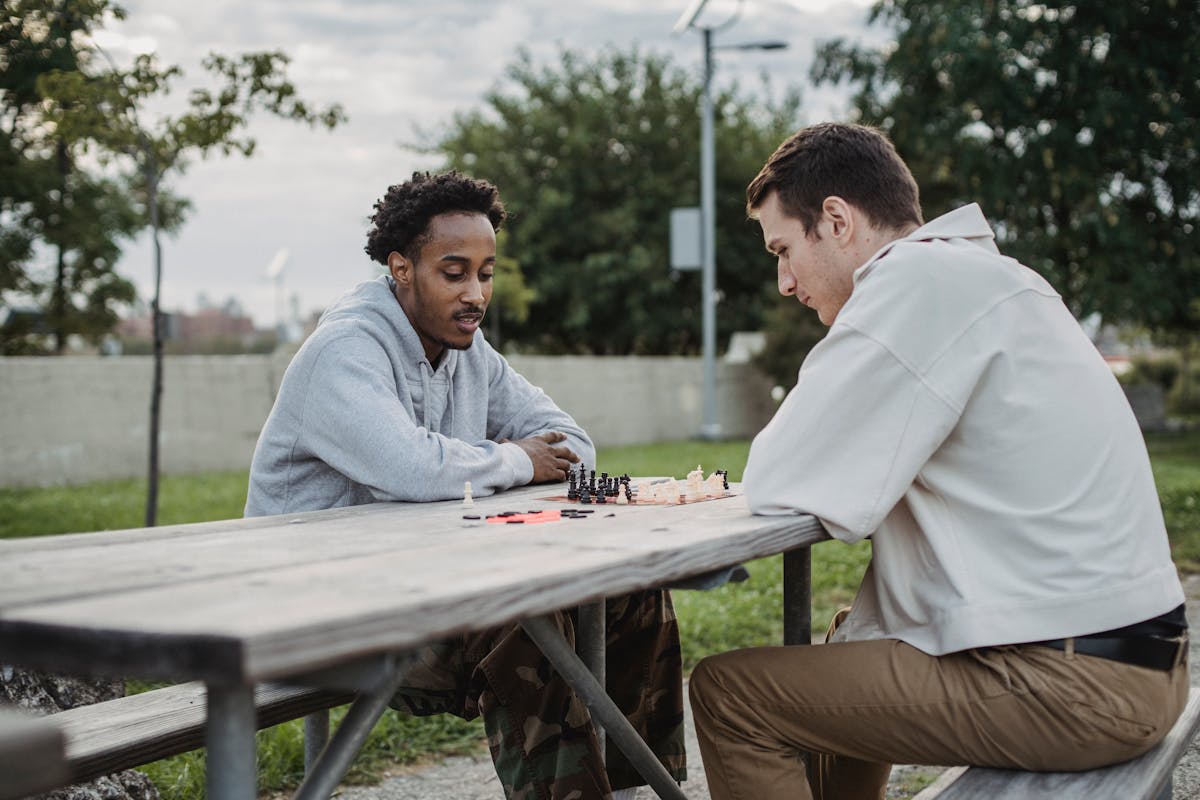 10 Subtle Phrases People Use When They Secretly Don’t Like You 4 Side view of serious young guy playing chess with African American friends while spending time in city park
