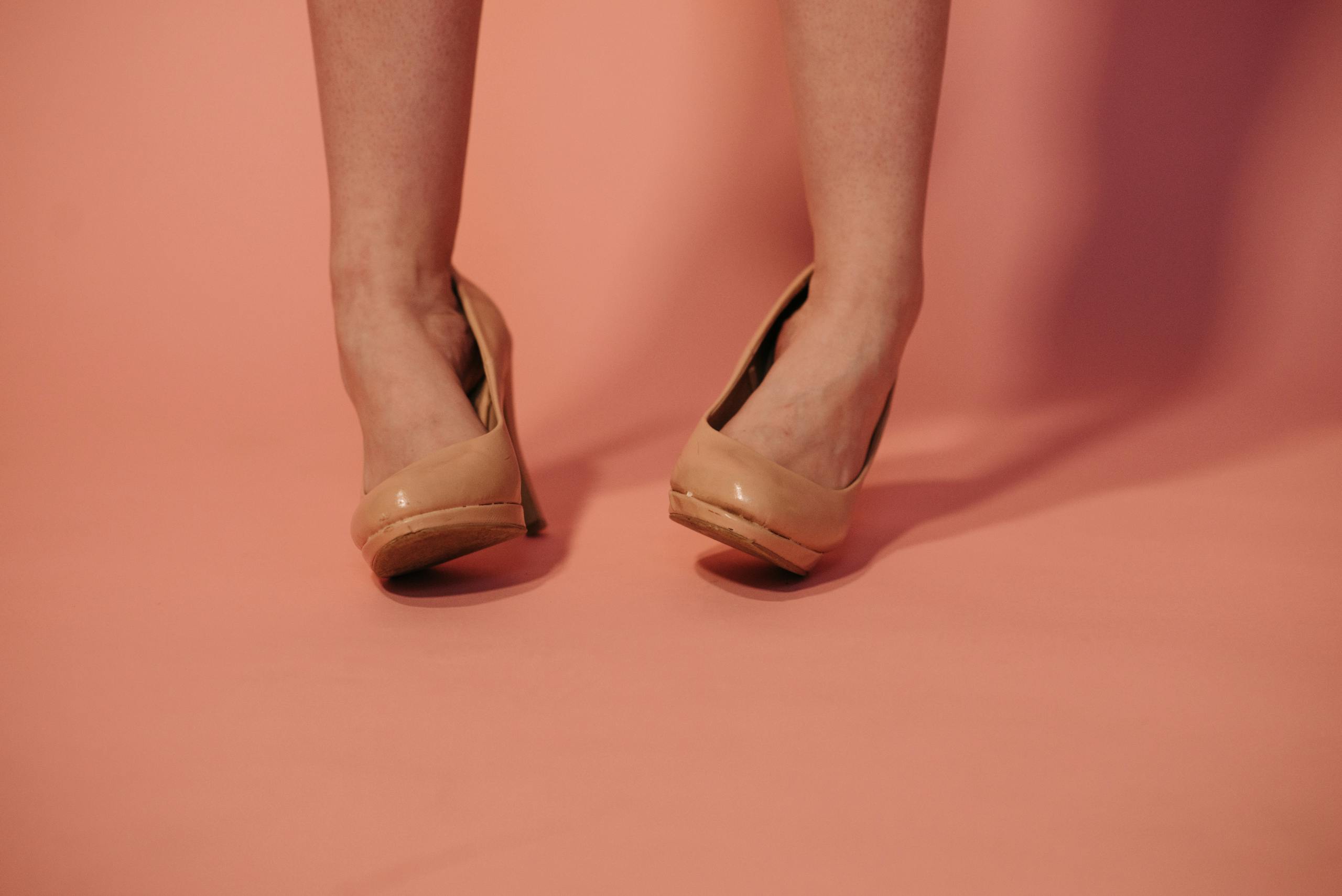 Stylish women's legs with beige high heels on a pink background. Perfect for fashion concepts.