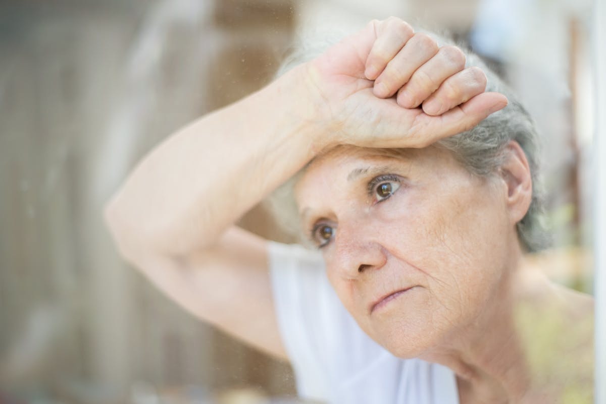 Thoughtful senior woman gazing through a window, symbolizing solitude and reflection.