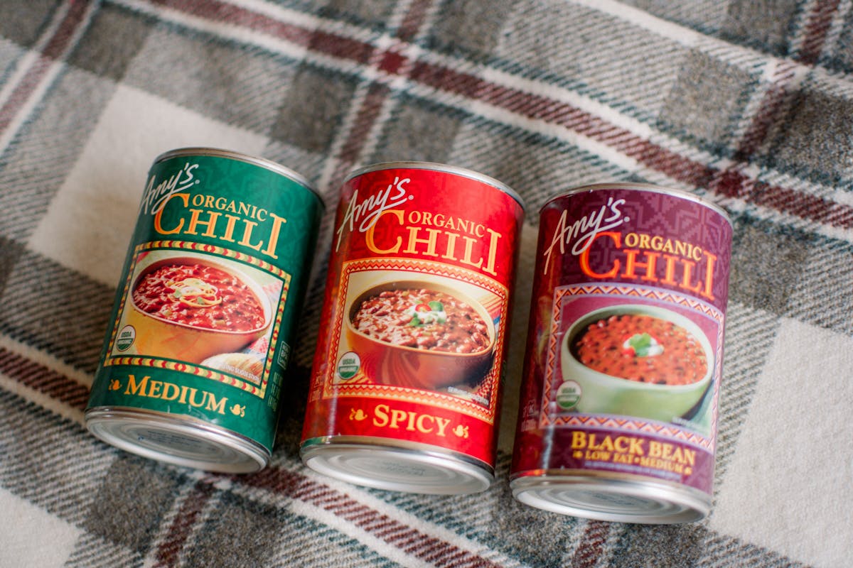 Three varieties of Amy's Organic Chili cans on a plaid picnic blanket.