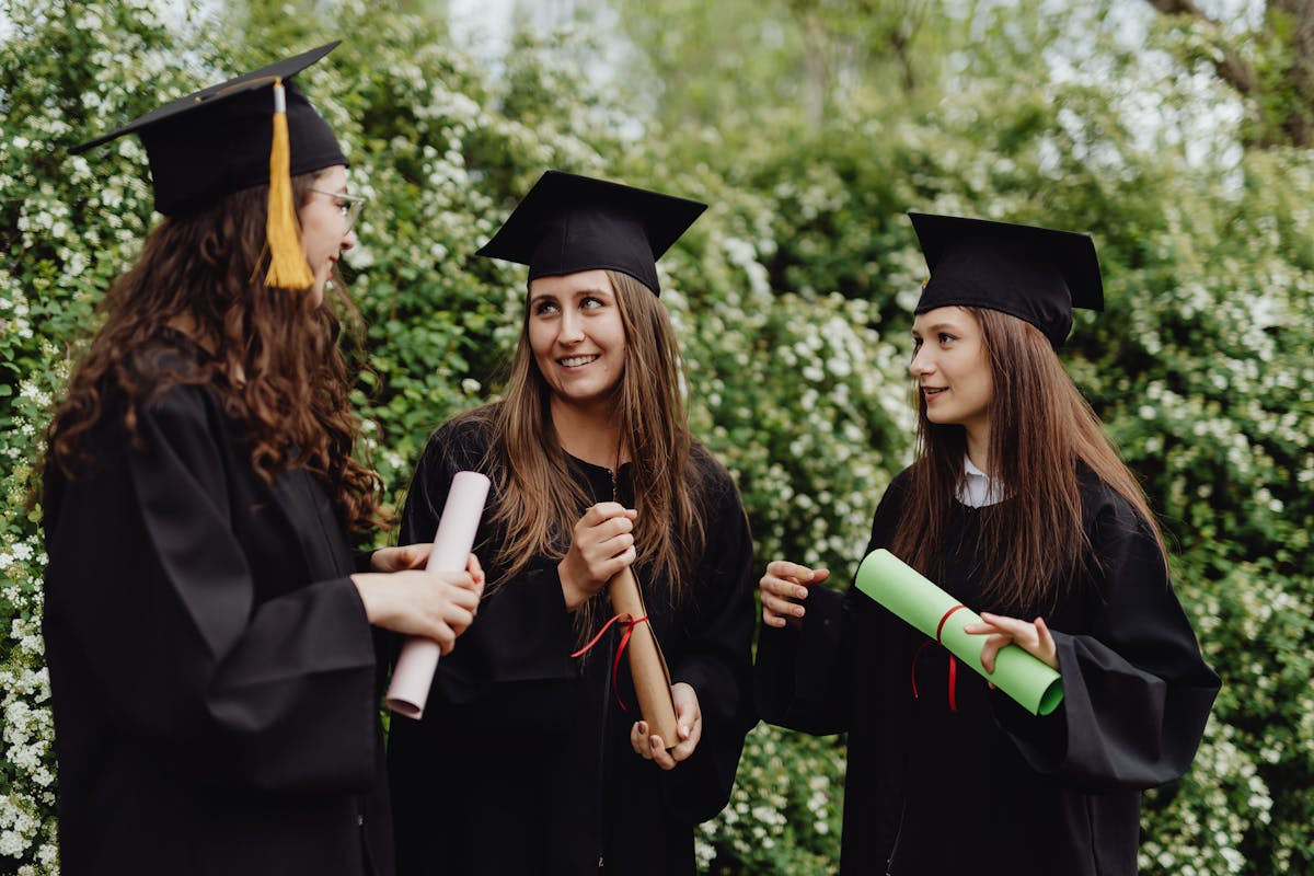 Three young women in caps and gowns celebrate their graduation with diplomas outdoors.