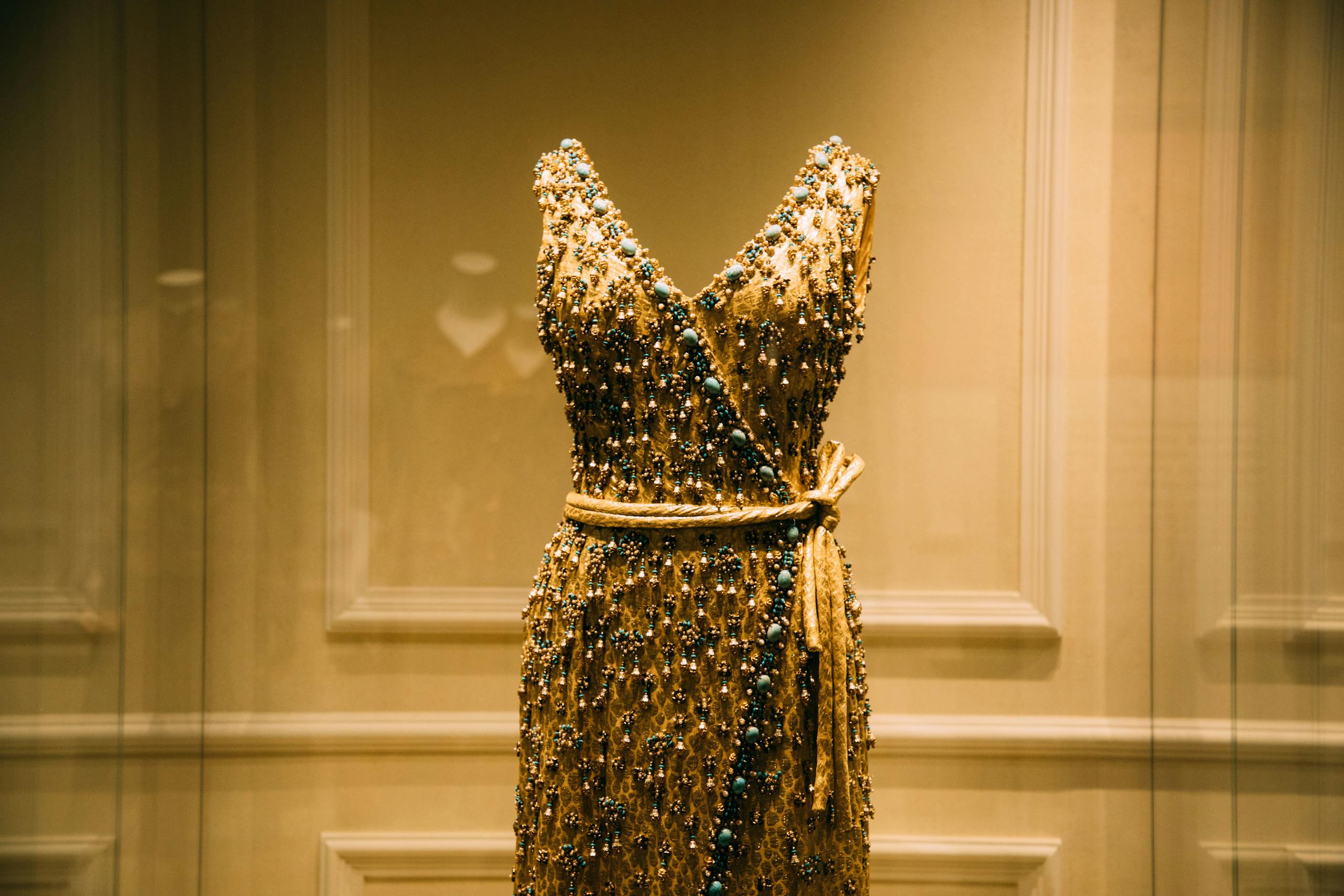 Through glass view of bright old style dress with pearls and belt in museum