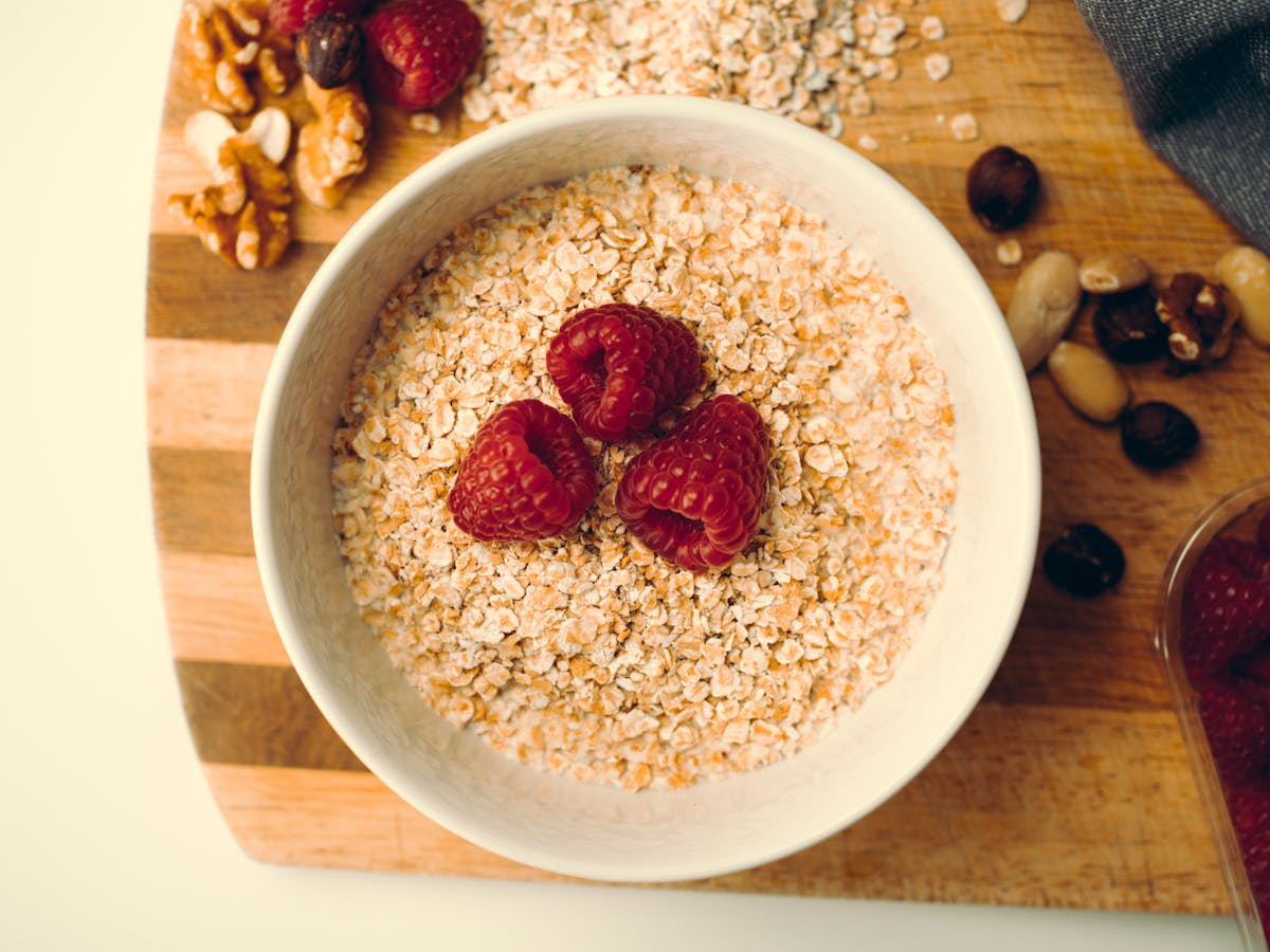 Top view of a white bowl with oatmeal, raspberries, and nuts on a wooden board, perfect for a healthy breakfast.