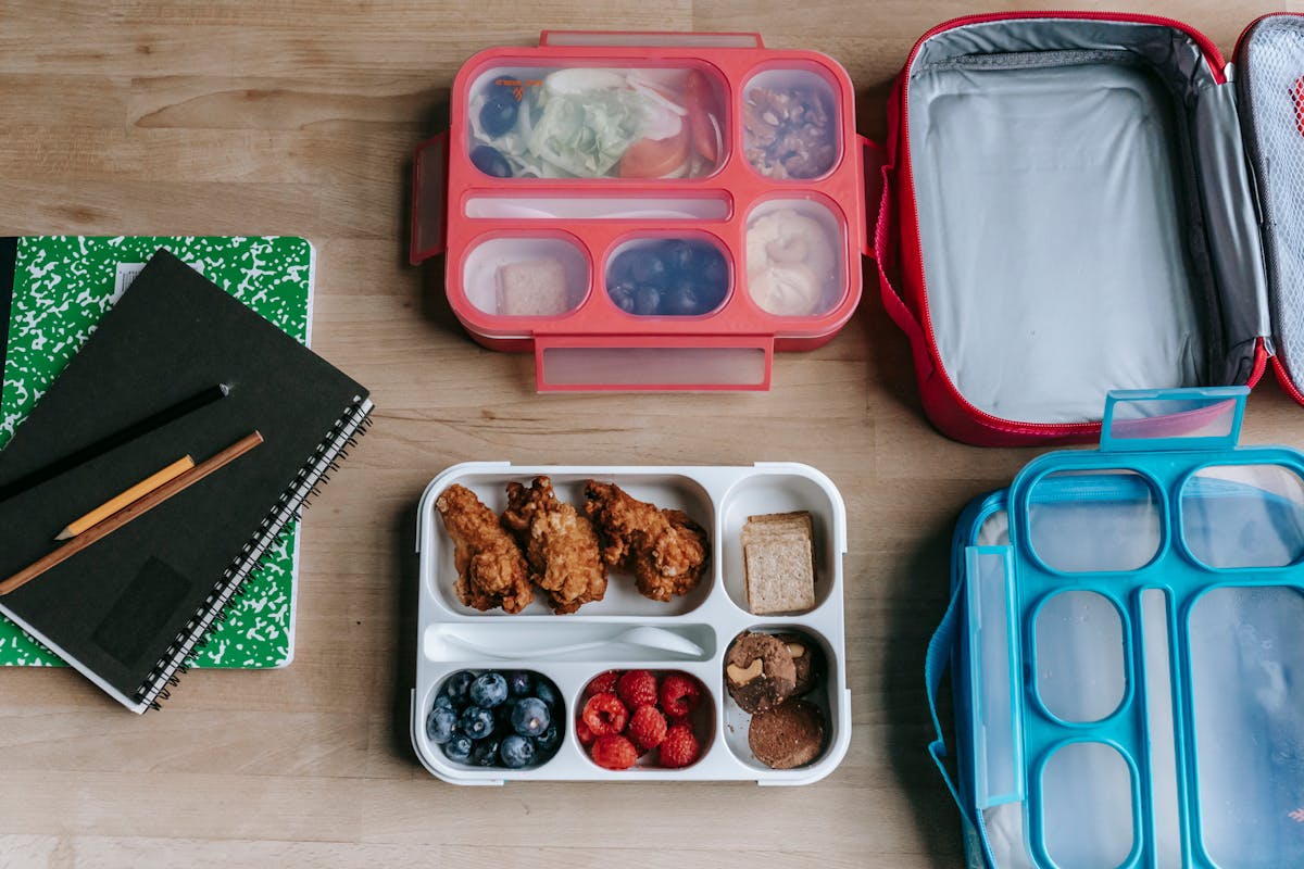 12 Family Meal Ideas That Save Parents From Mealtime Chaos 3 Top view of composed plastic lunchboxes near copybooks under pencils on wooden table