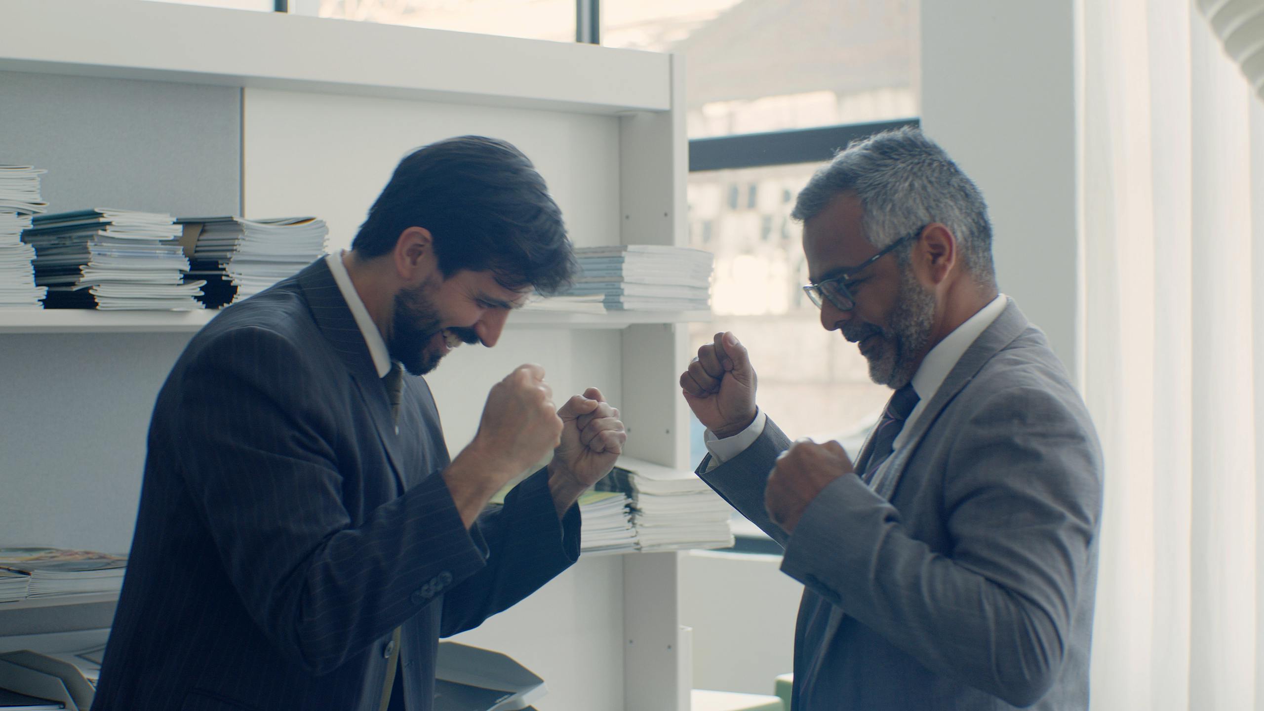 10 Ugly Truths About American Work Culture Nobody Wants to Admit 3 Two businessmen in suits celebrating success with fists raised in a modern office setting.