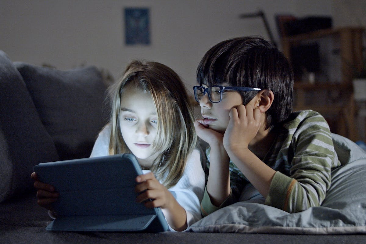 Two children using a tablet in a cozy home setting, engaging in screen time.