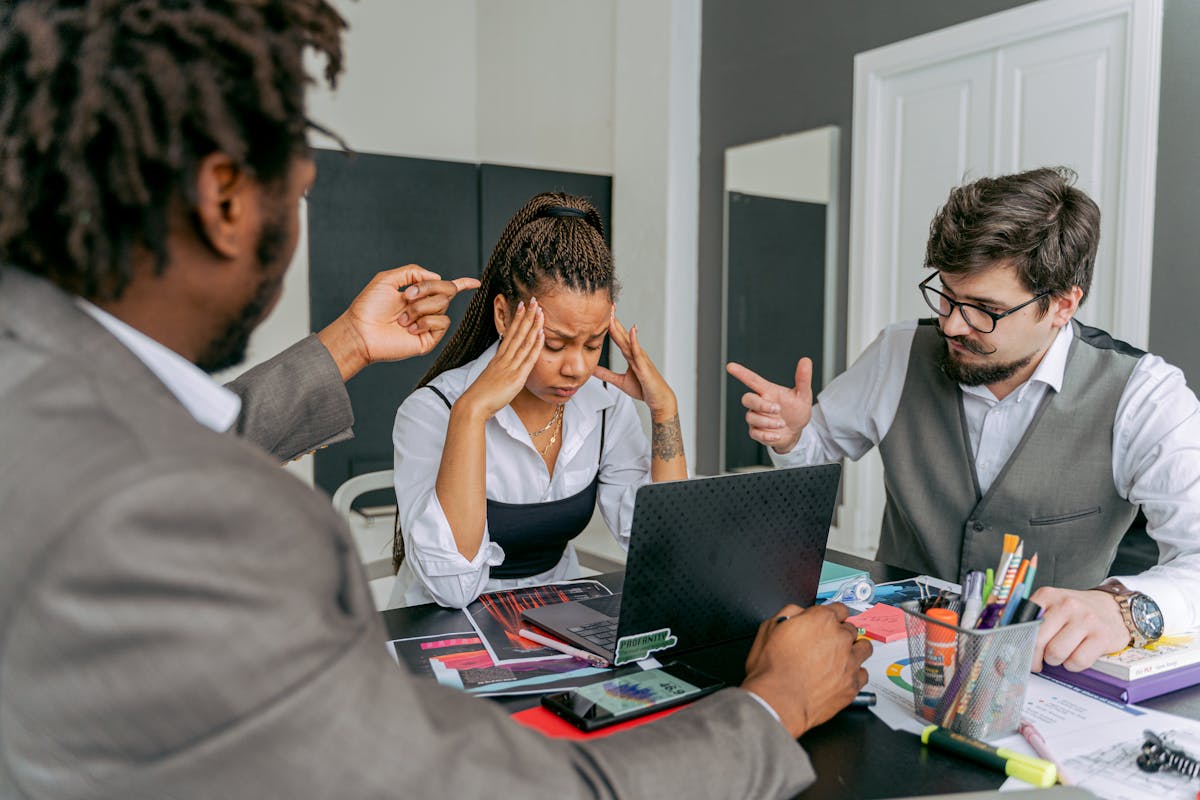 Two colleagues stress a coworker during an intense team meeting in a modern office setting.