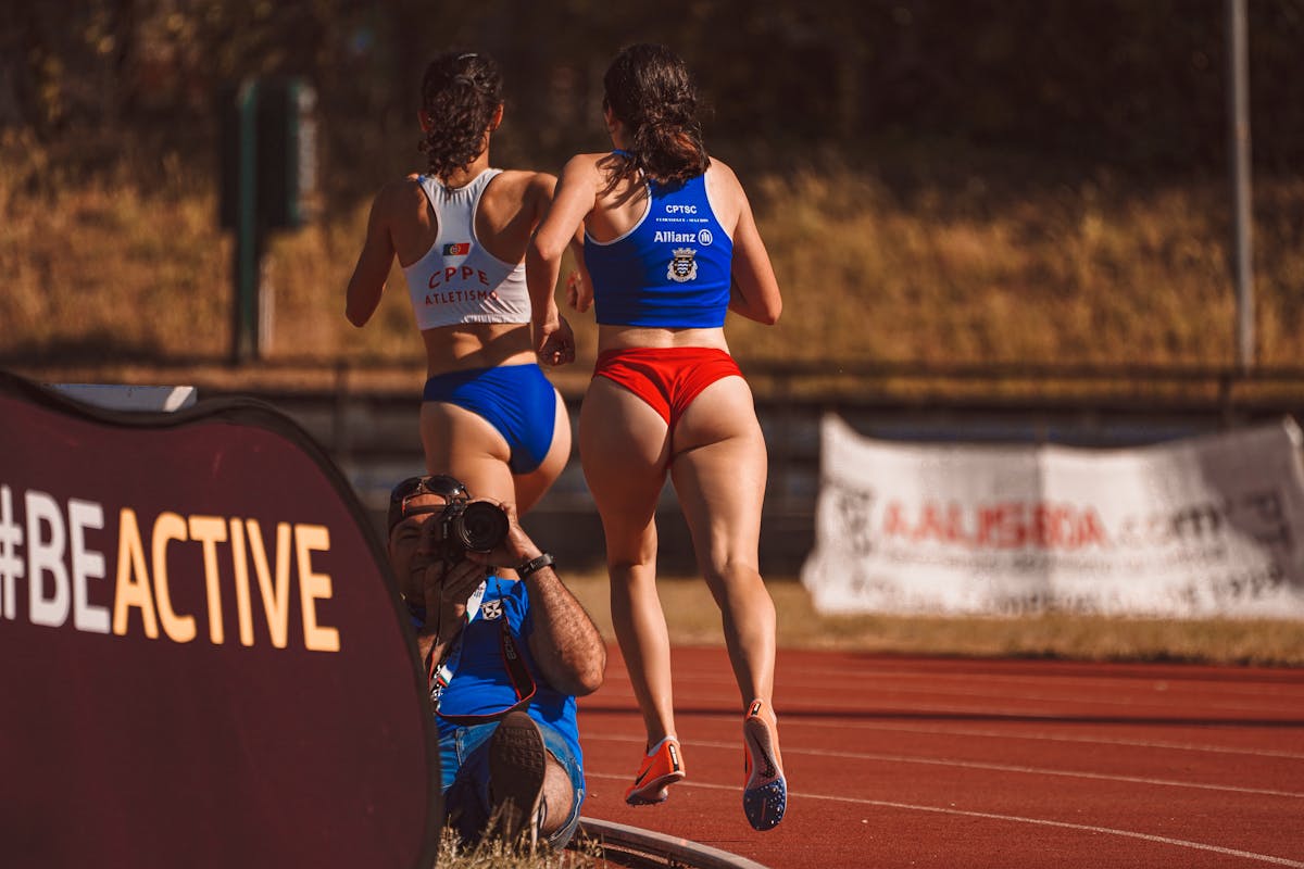 7 Disturbing Thoughts Some Men Admit Having About Revealing Sports Uniforms 2 Two female athletes running on a track during a sports competition, captured by a photographer.
