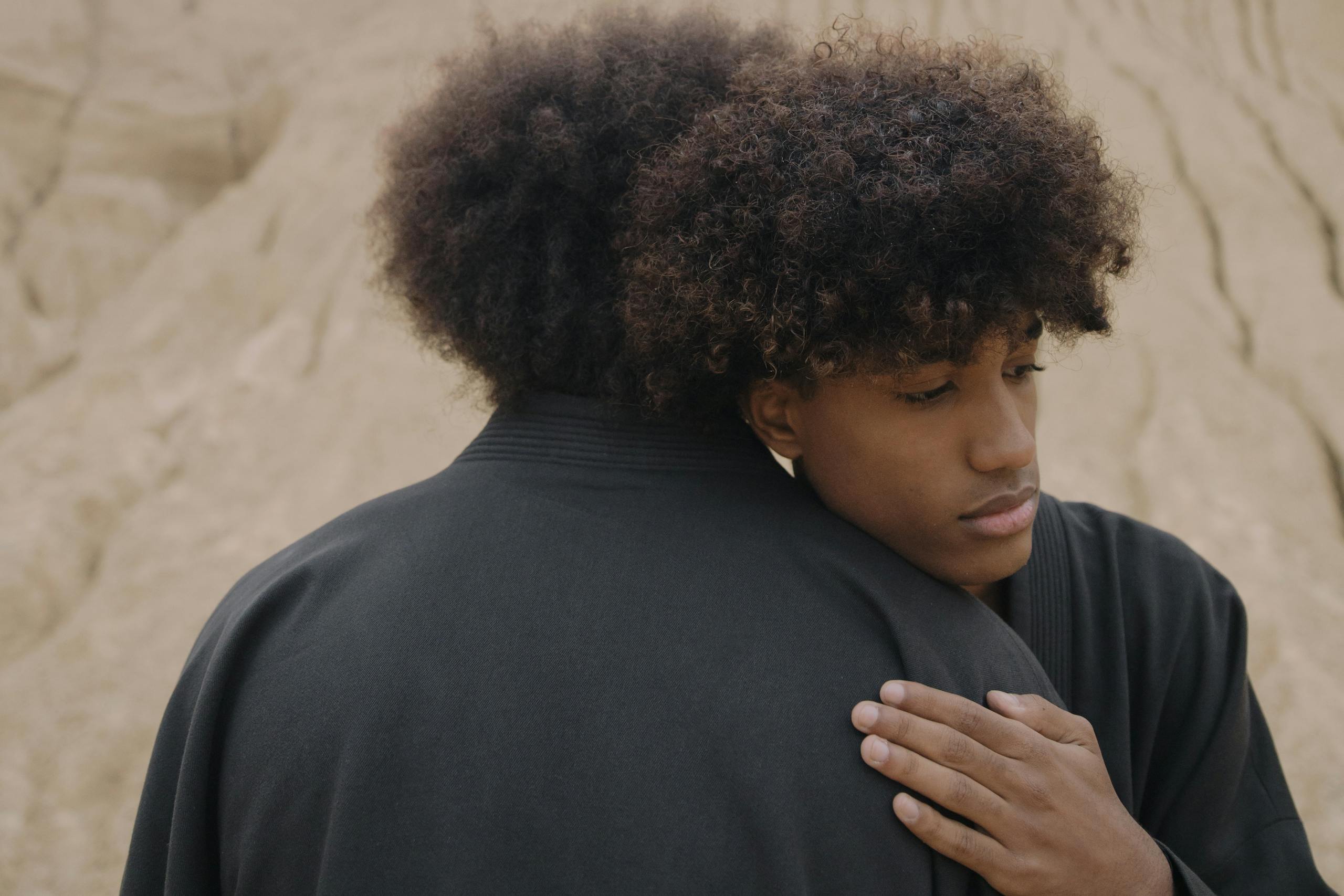 Two men embracing with a desert landscape in the background, conveying a sense of support and connection.