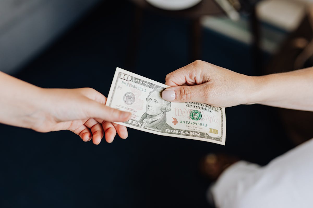 8 Tax Fights That Could Financially Ruin Millions of Americans in 2026 4 Two people exchanging a ten dollar bill in a close-up hand-to-hand transaction.