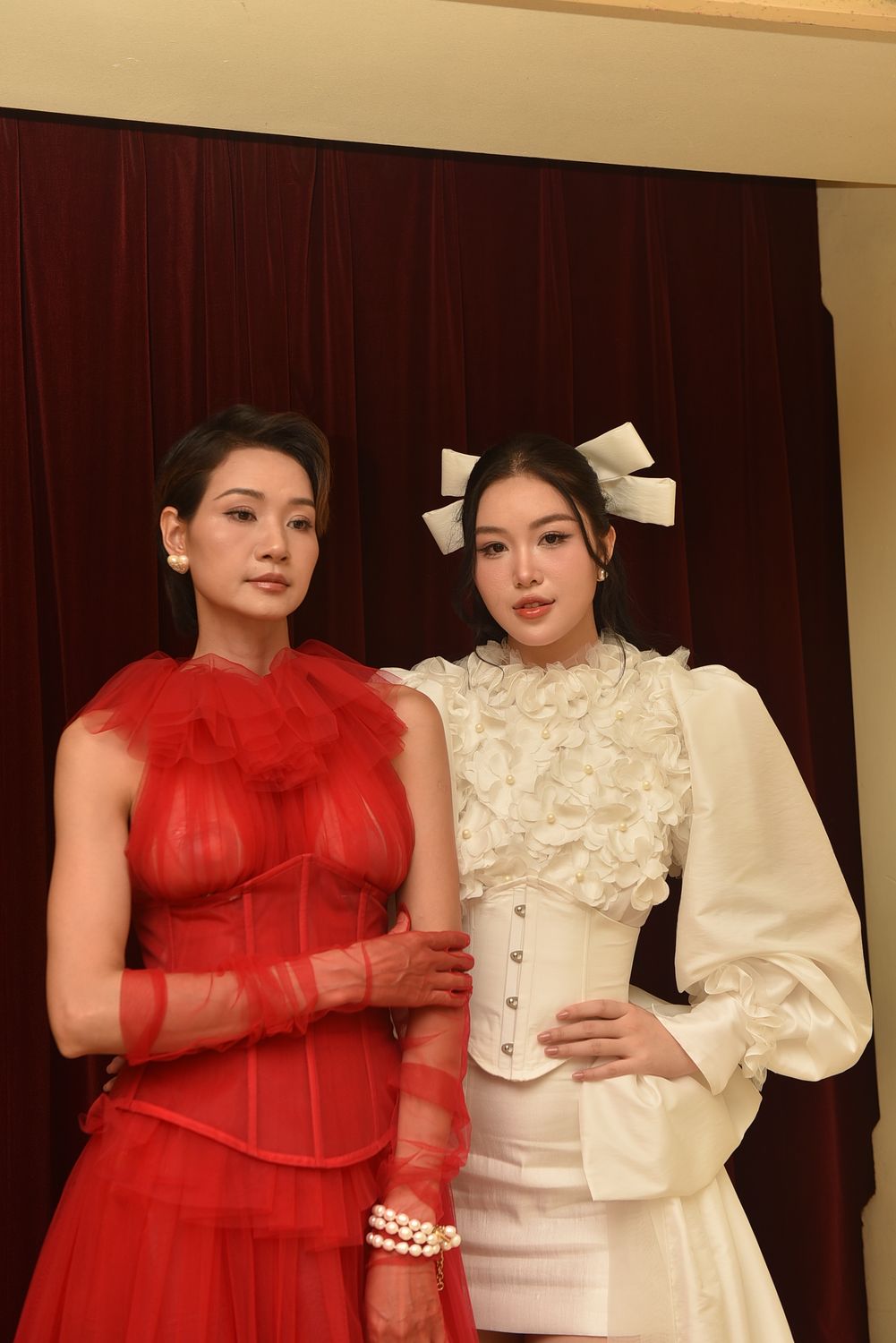 Two women in stylish red and white formal dresses posing elegantly indoors.