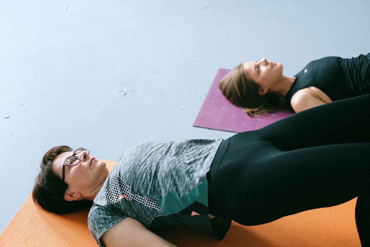 50 Isn’t Too Late, But These 8 Mistakes Make It Harder 3 Two women performing floor exercises on yoga mats indoors in a fitness studio.