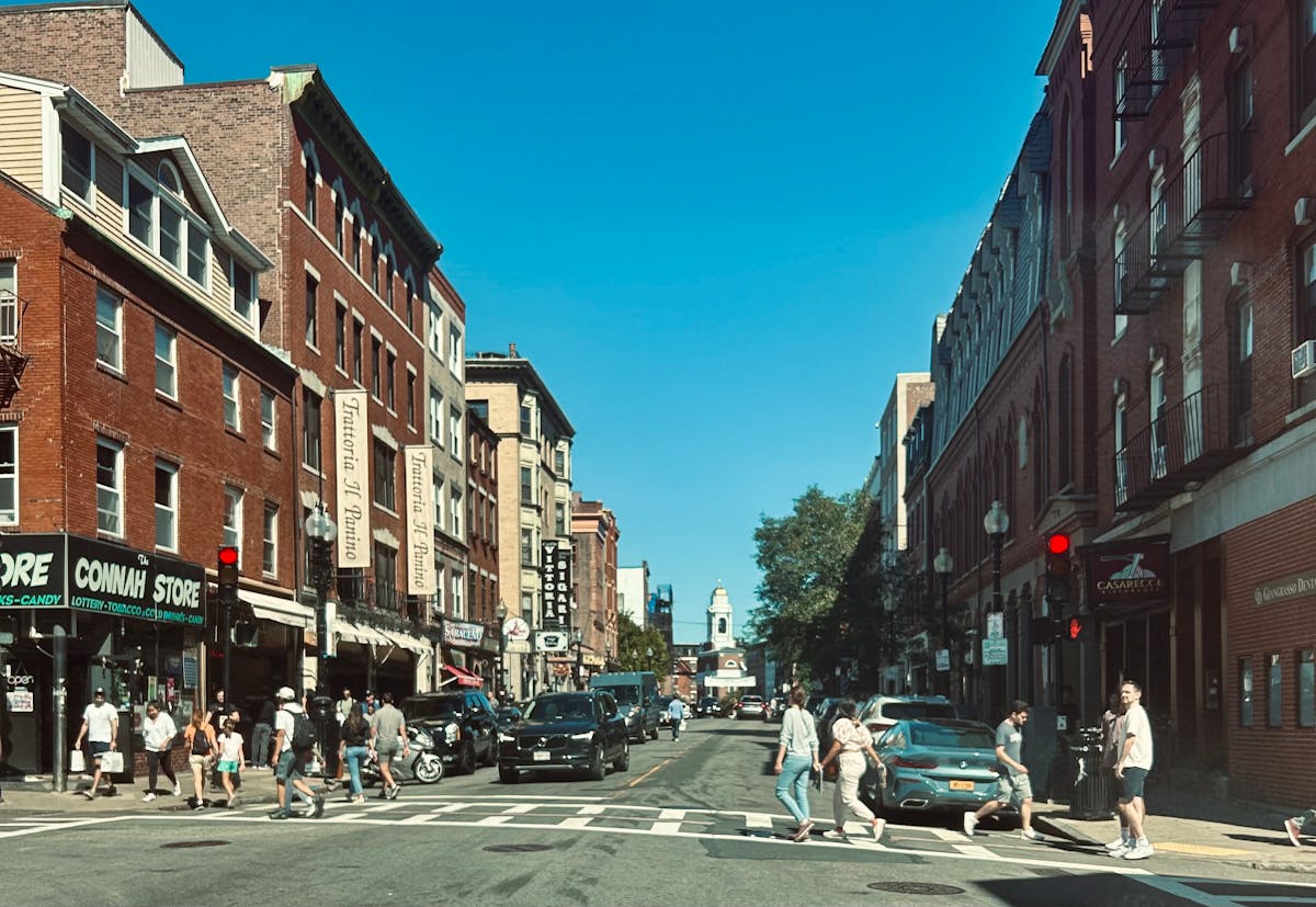 Vibrant street view of Hanover Street in Boston's North End with pedestrians and red brick buildings.