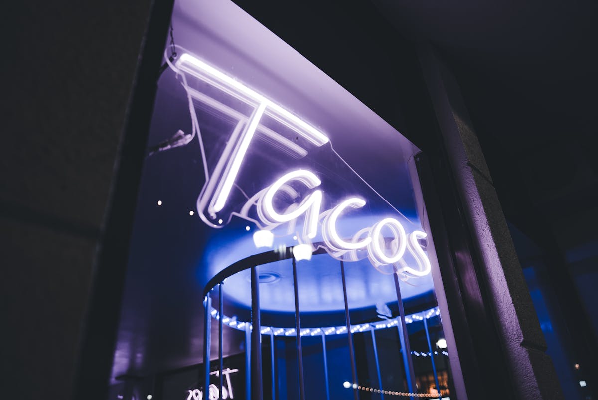 Vivid neon taco sign glowing brightly against a dark night street setting.