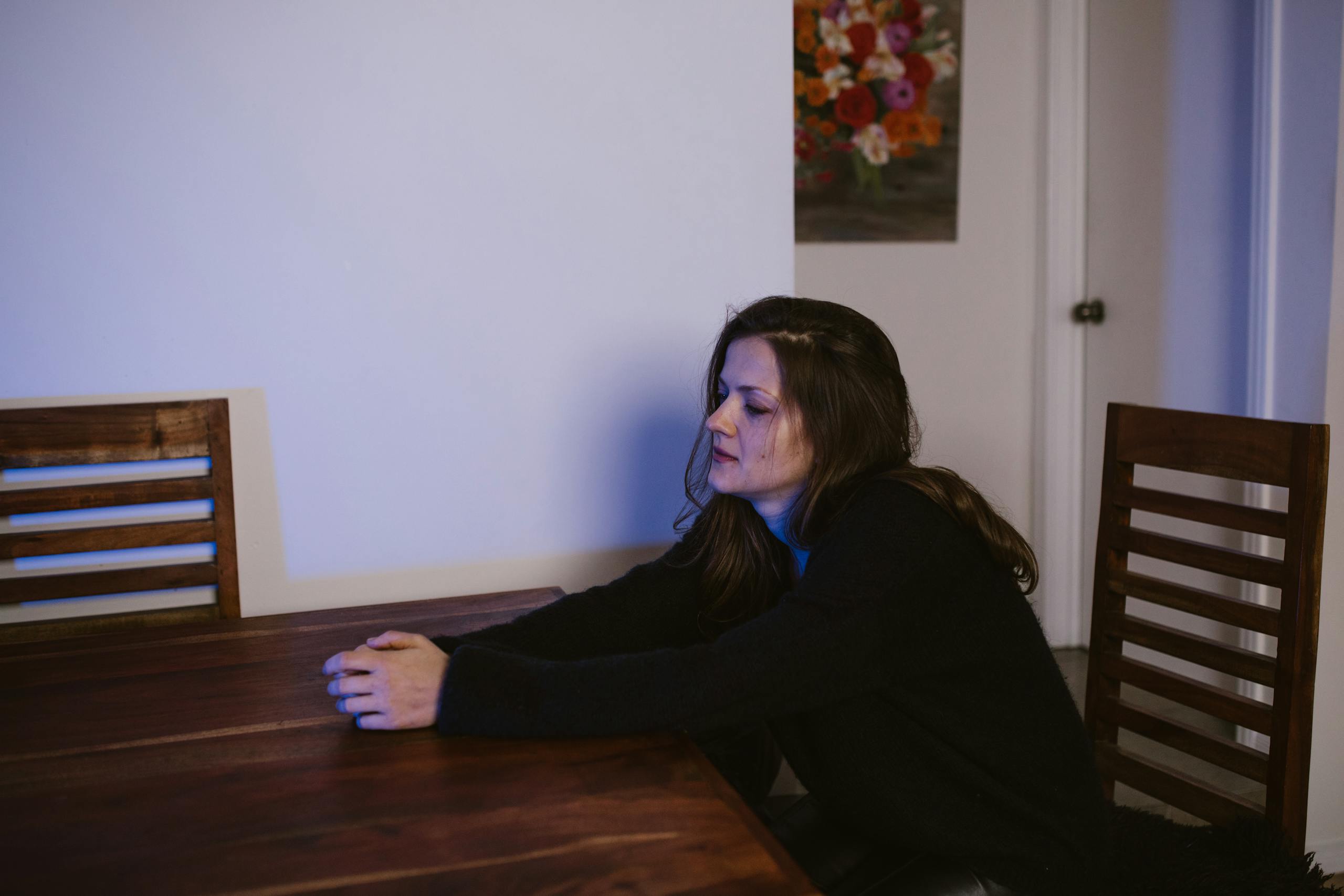 10 Harsh Truths About Why Church No Longer Feels Like Home to Some Americans 2 Woman sitting alone at a dining table, contemplating in a dimly lit room.