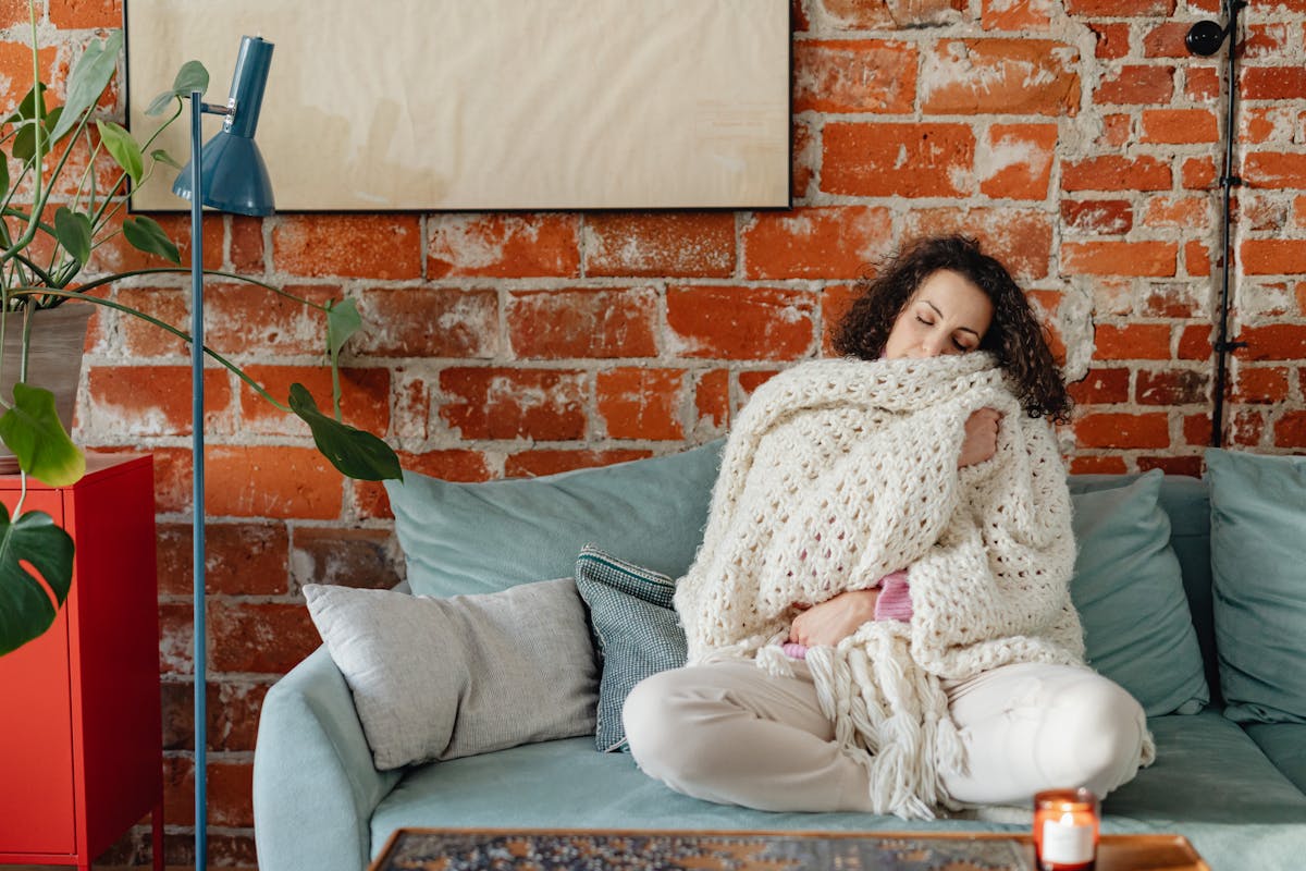 10 Alarming Symptoms of Hantavirus You Need to Recognize Amid the Ship Outbreak 3 Woman sitting comfortably on a couch with a knitted blanket in a warm indoor setting.