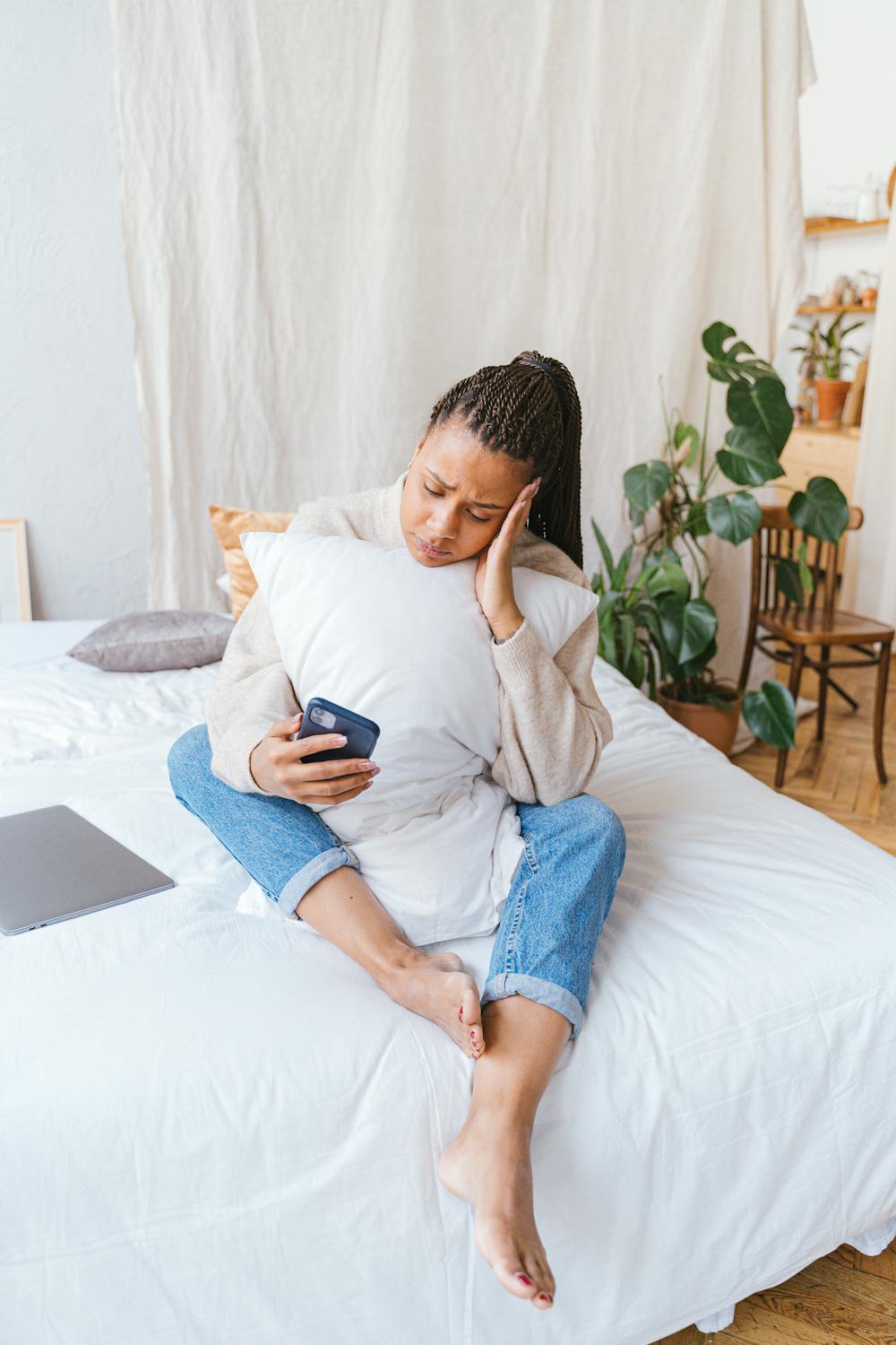 10 Toxic Guilt Traps Women Need To Stop Falling For 2 Woman sitting on bed, holding smartphone, looking thoughtful. Modern home setting.