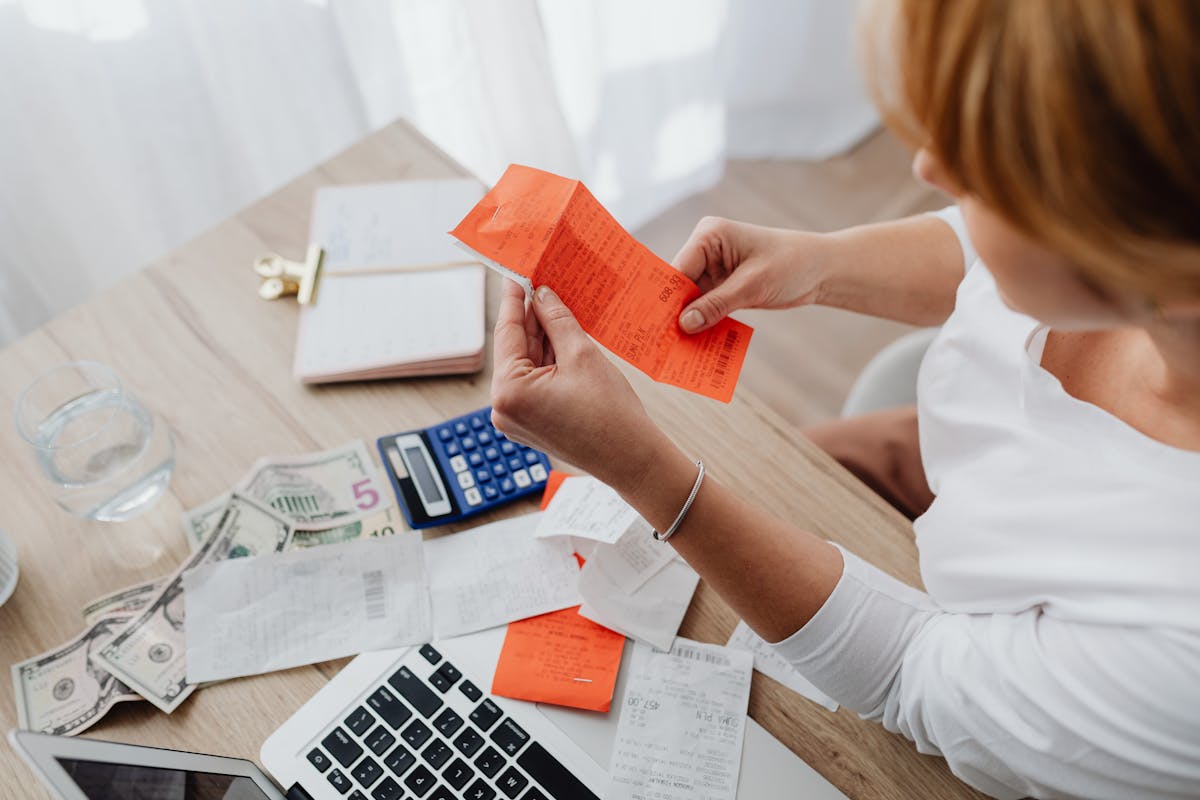 A woman using a calculator and receipts at a home office desk for financial management.