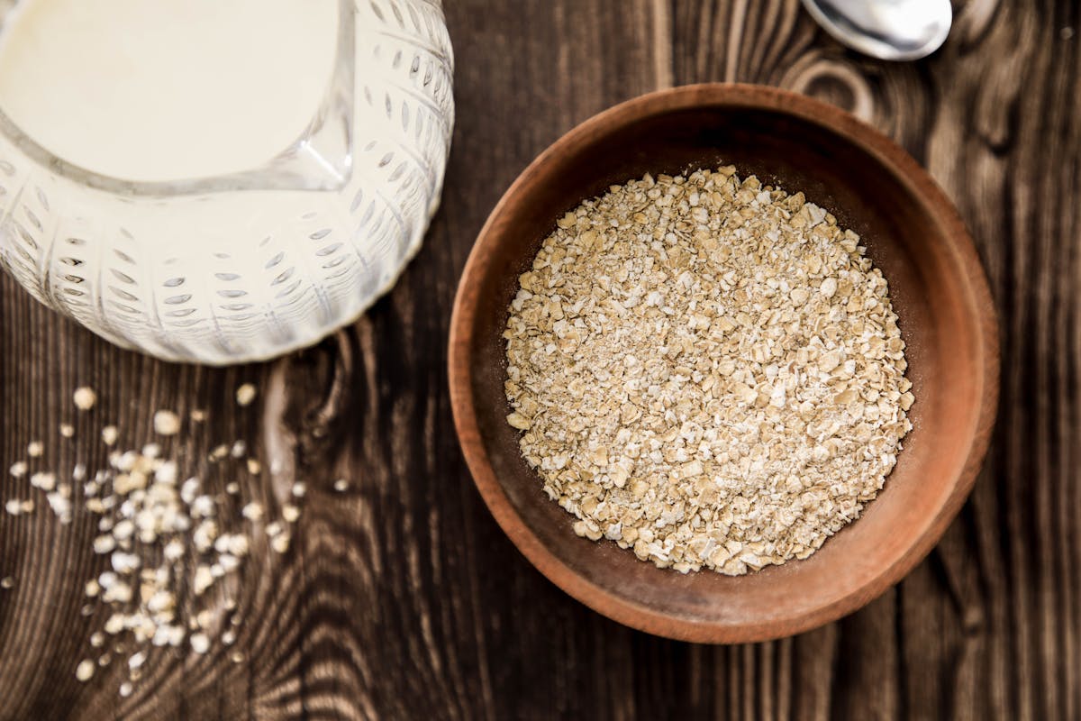 Wooden bowl of oats with milk jug on rustic table. Ideal for health-focused breakfast imagery.